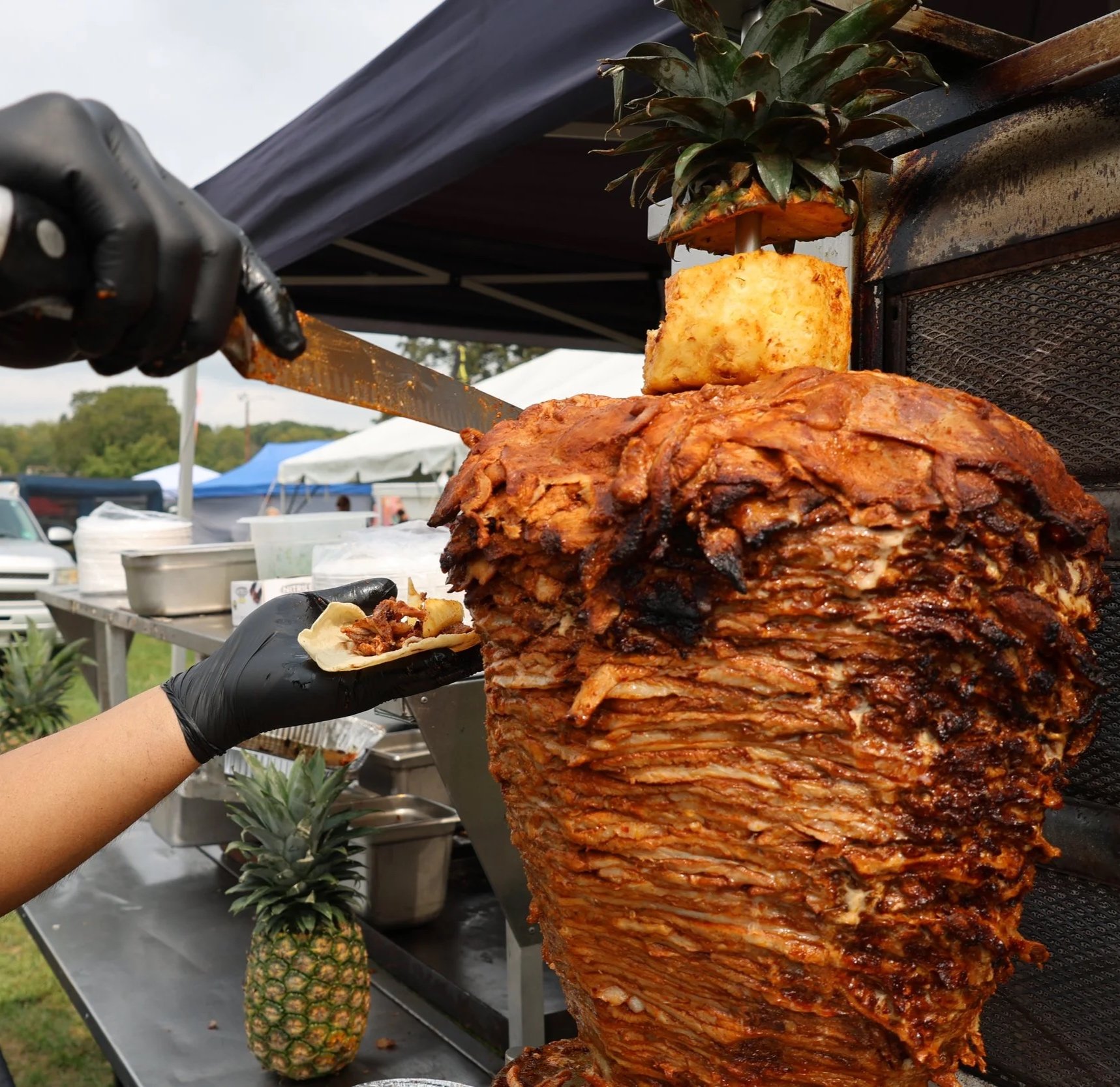 Whole pineapple and a large rotisserie pig with crispy, golden-brown skin being prepared at an outdoor food festival.