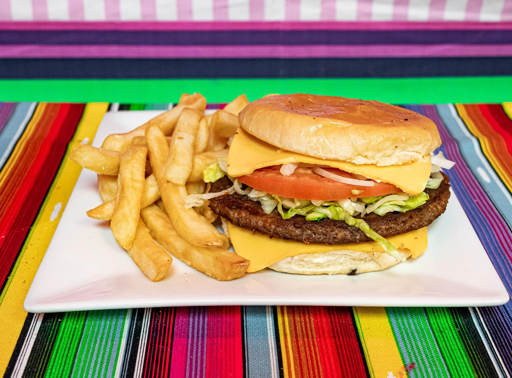 A cheeseburger with lettuce, tomato, and onion on a bun, served with French fries on a decorative plate.