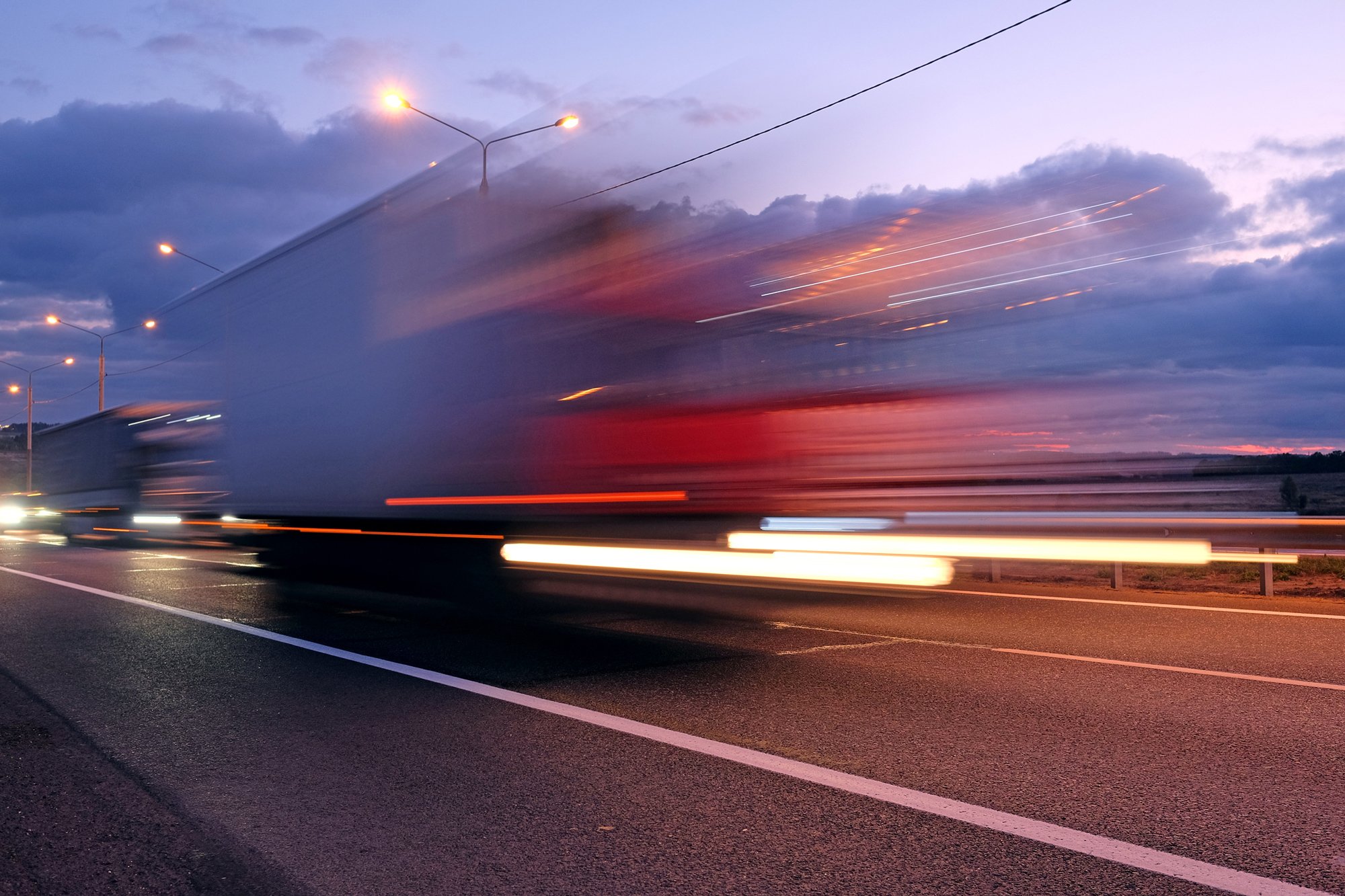 A truck moving quickly on a highway at dusk with blurred lights and sky, creating motion blur.