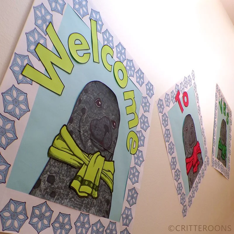 Colorful posters featuring a cartoon otter wearing a yellow scarf and the word "Welcome," decorated with snowflakes, displayed on a wall.