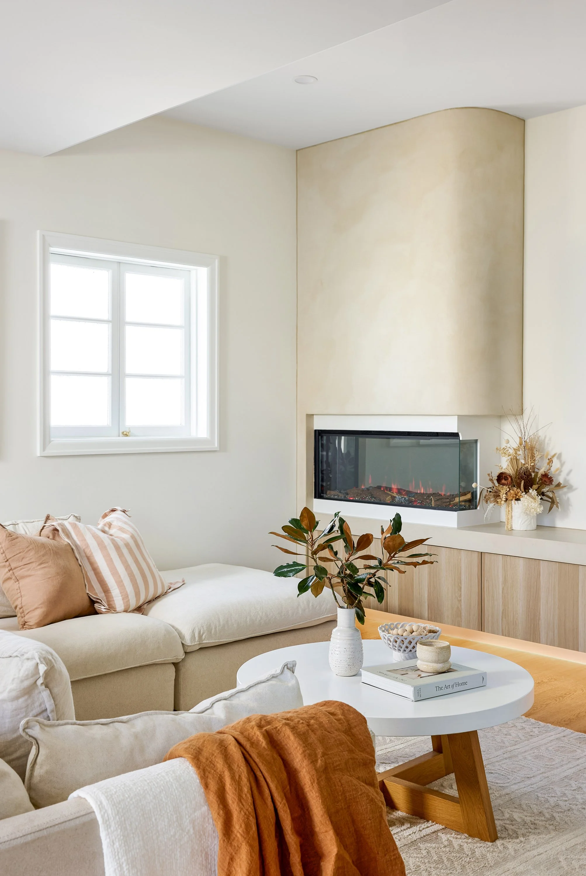 Living room with beige sofa, white coffee table, fireplace, window, and decorative plants and vases.