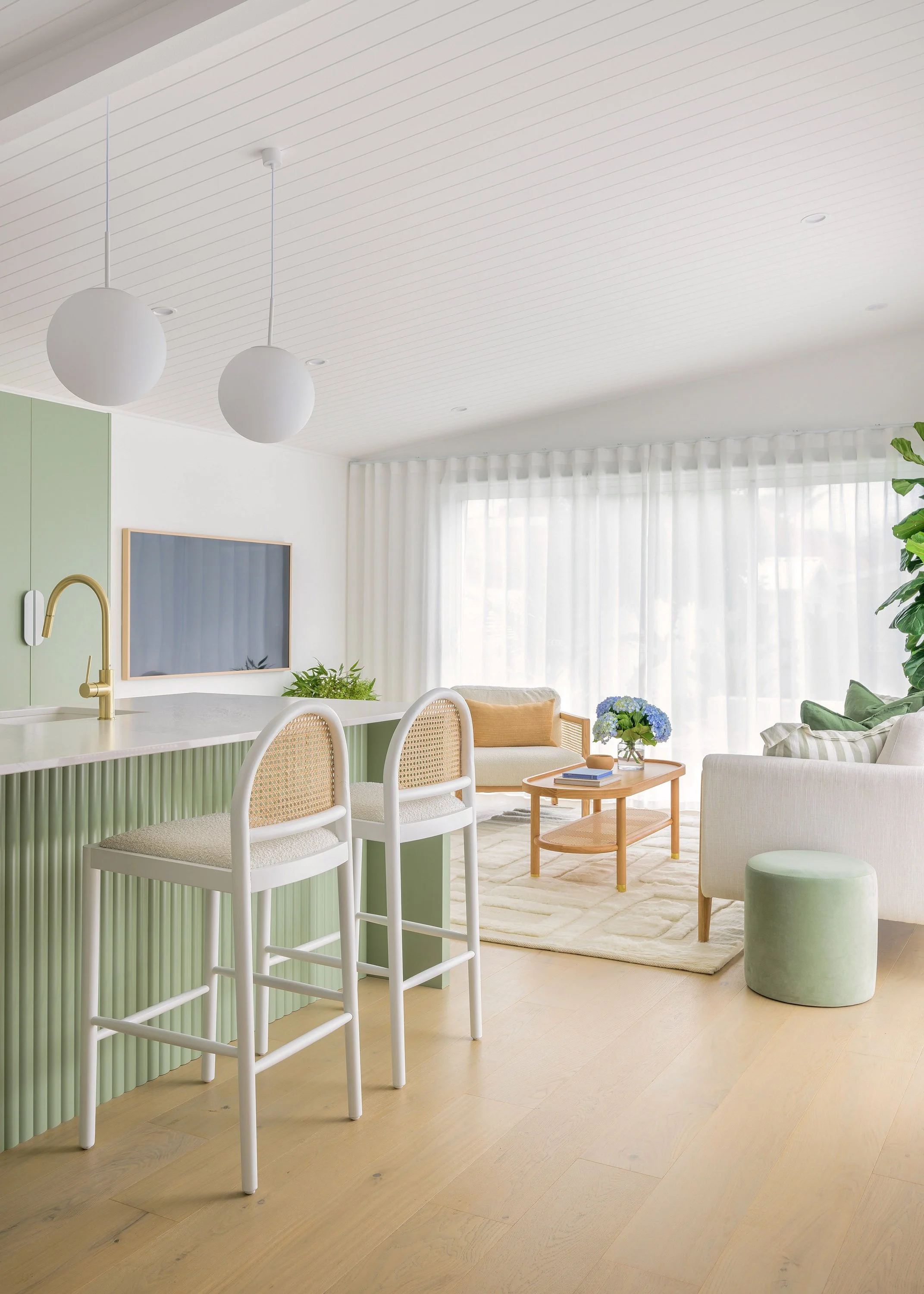 Bright, modern living room with white and green decor, white curtains, light wood furniture, and natural sunlight.