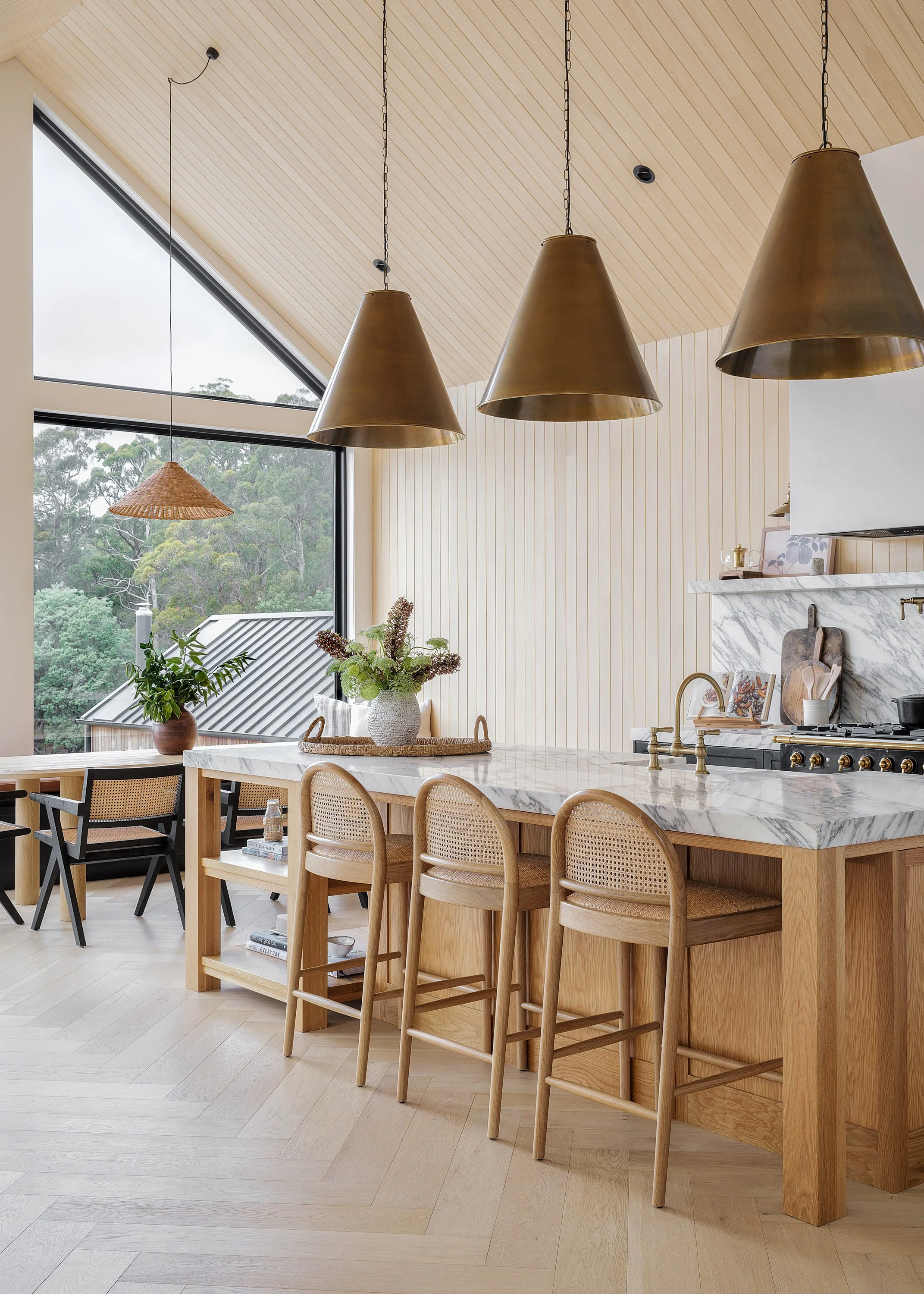 Modern kitchen with a marble island, wooden bar stools, pendant lights, large window, and minimal decor.
