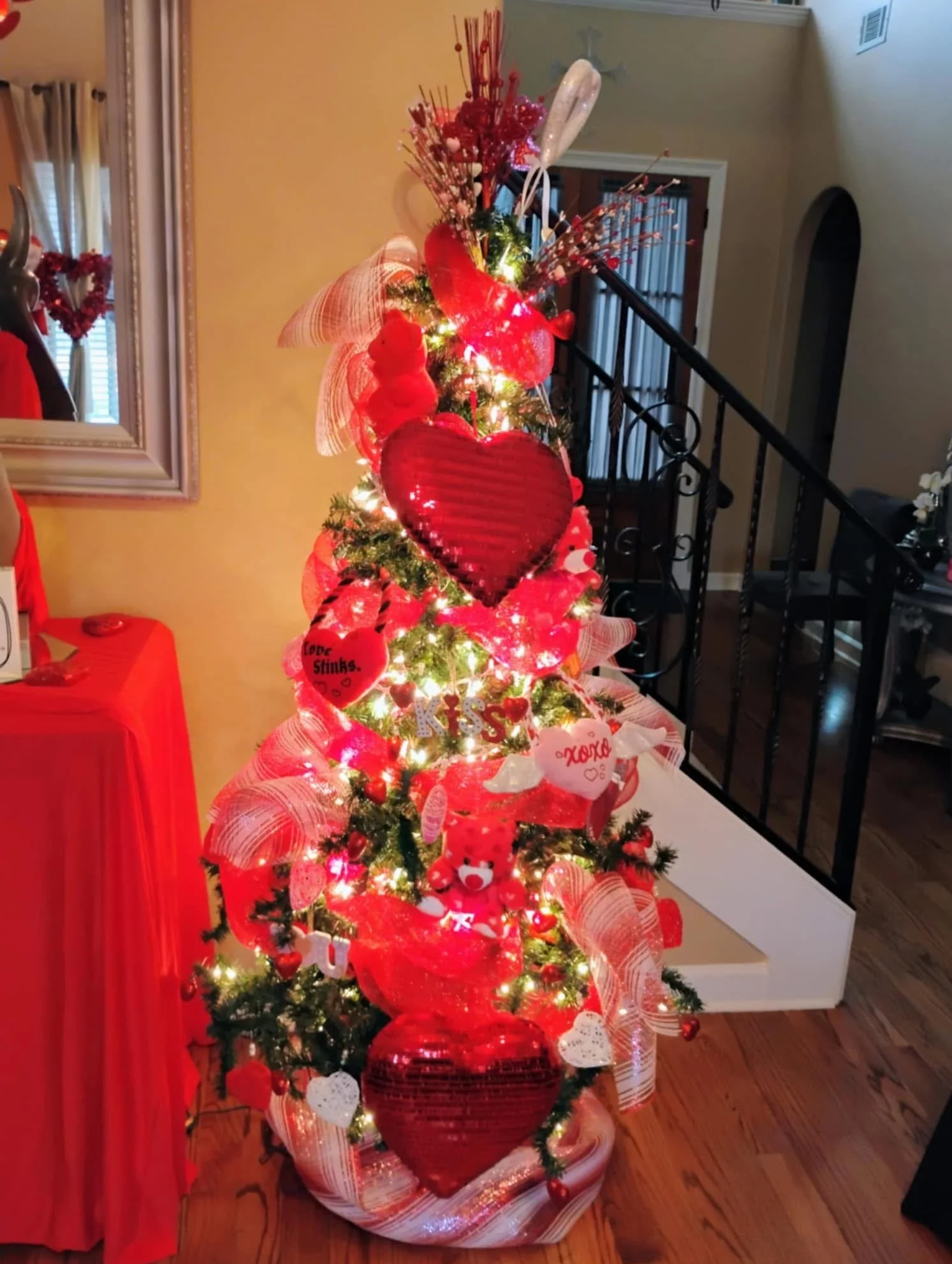 Decorated Christmas tree with red and white ornaments, ribbons, and lights inside a house.