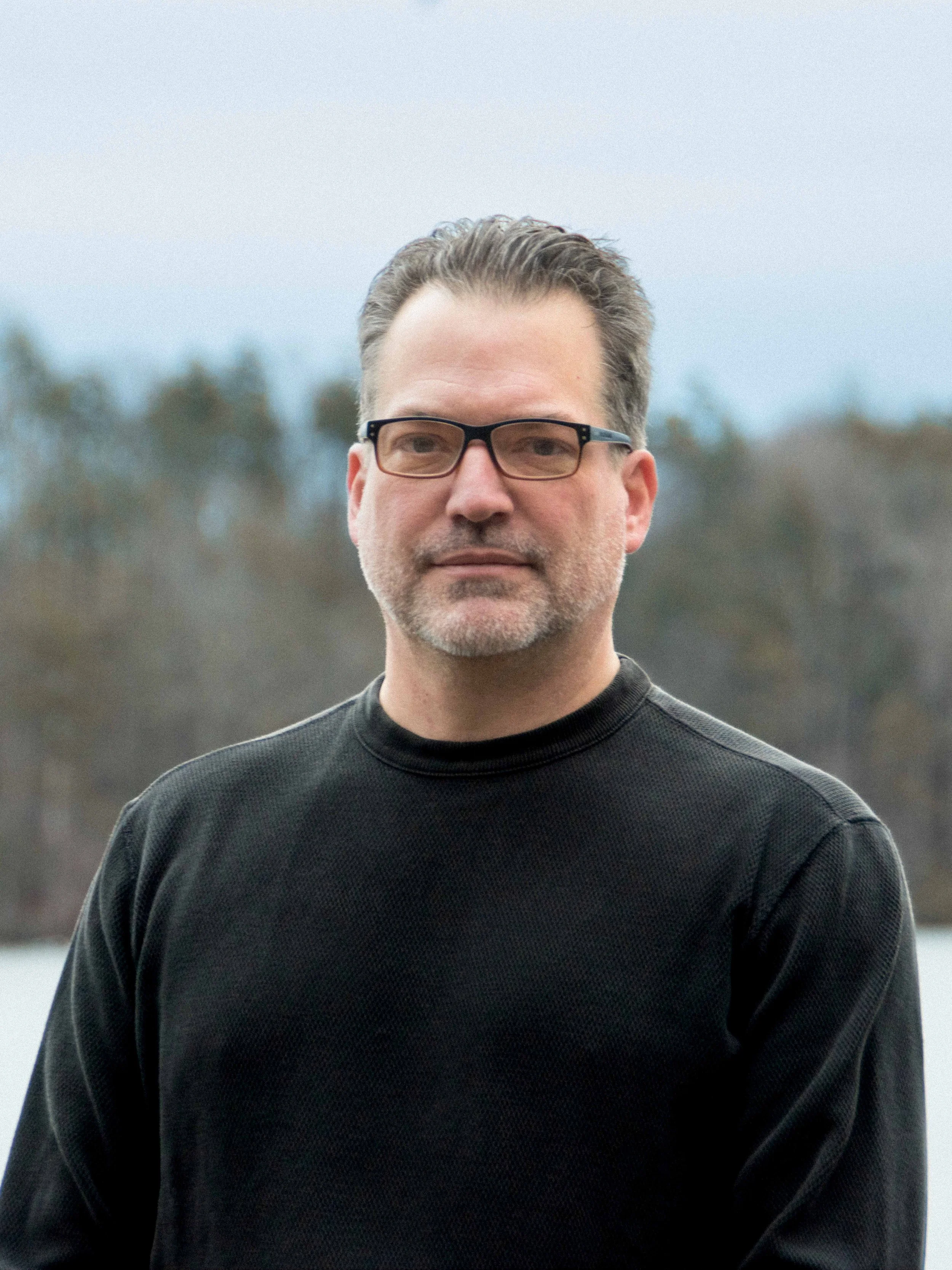 Portrait of Samuel Wykoff standing outdoors with a lake and wooded landscape in the background