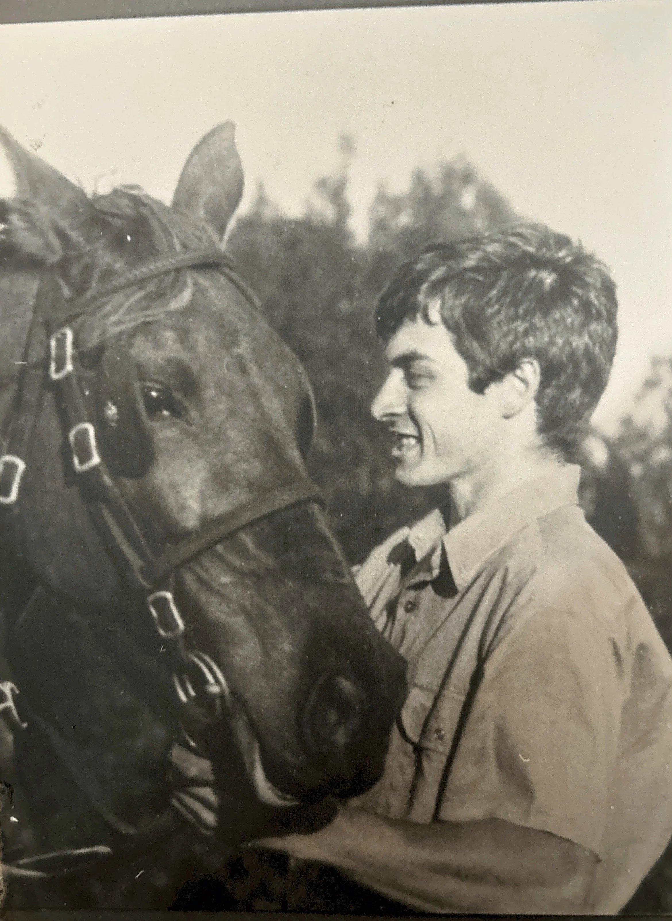 Cameron McDonald as A young man, smiling and leaning towards a horse, face close to the horse's face, outdoors. Vintage horse photo.
