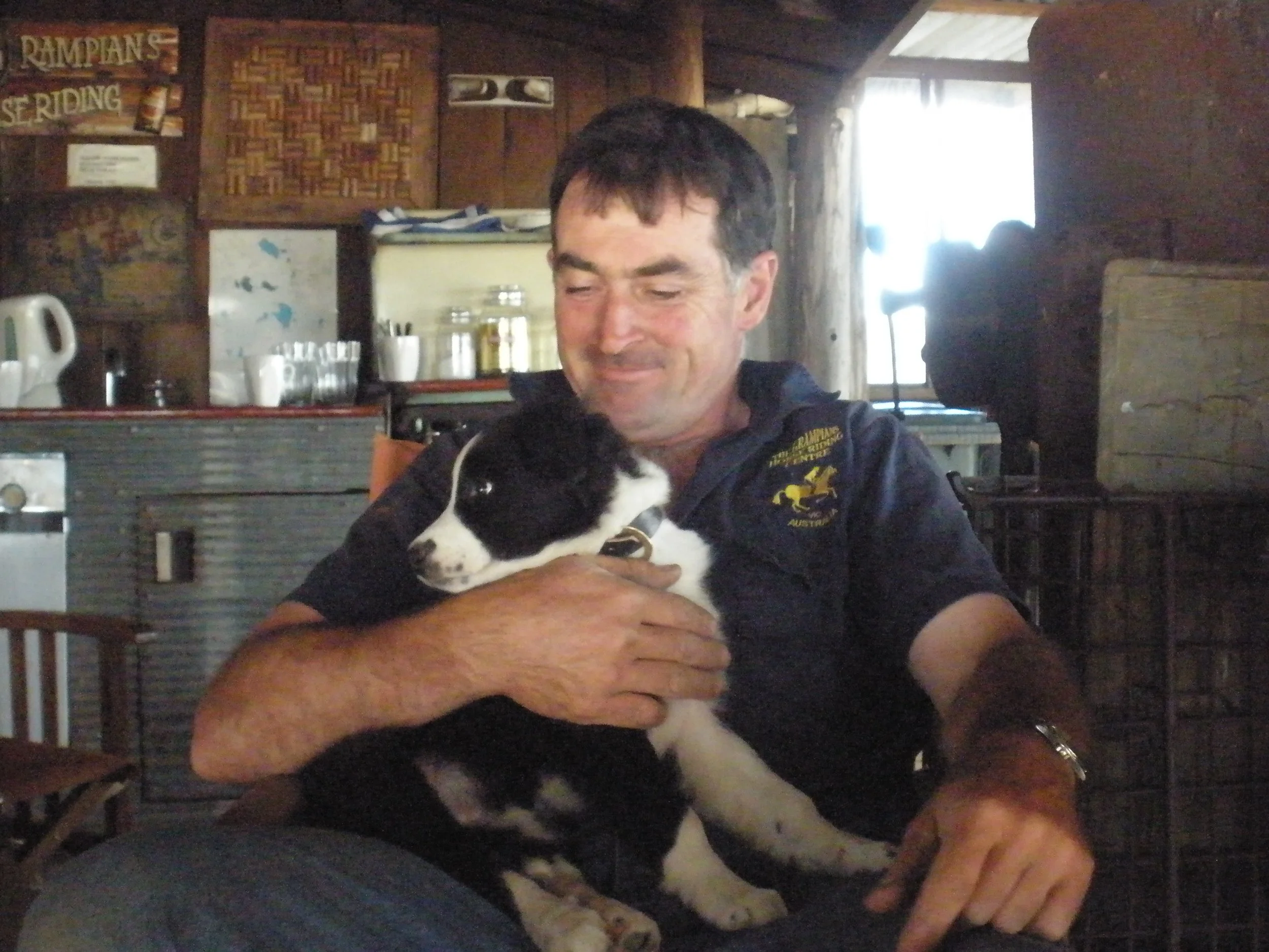 A man holding a black and white puppy in a cozy, wooden interior.