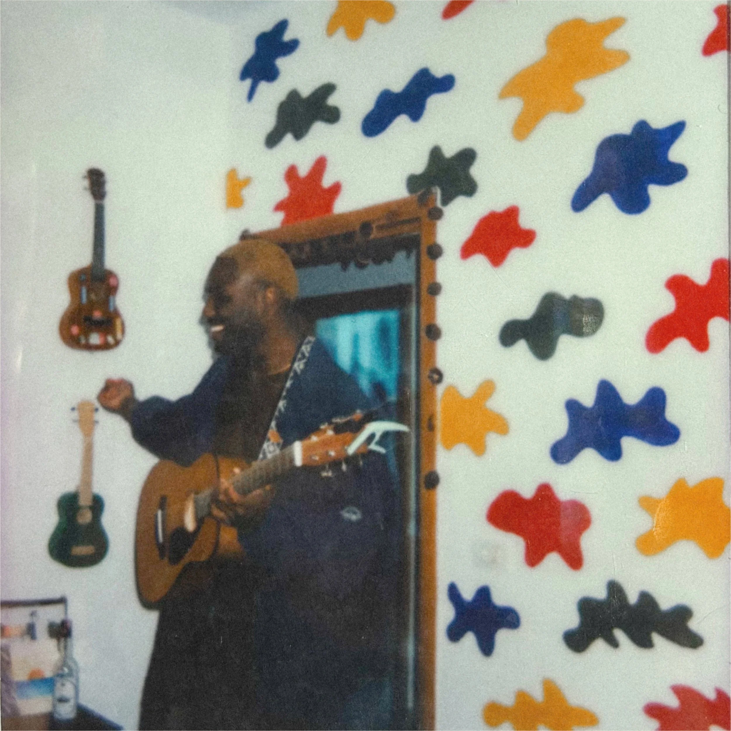 A man with blonde hair playing an acoustic guitar in a room decorated with colorful foam animal shapes on the wall.