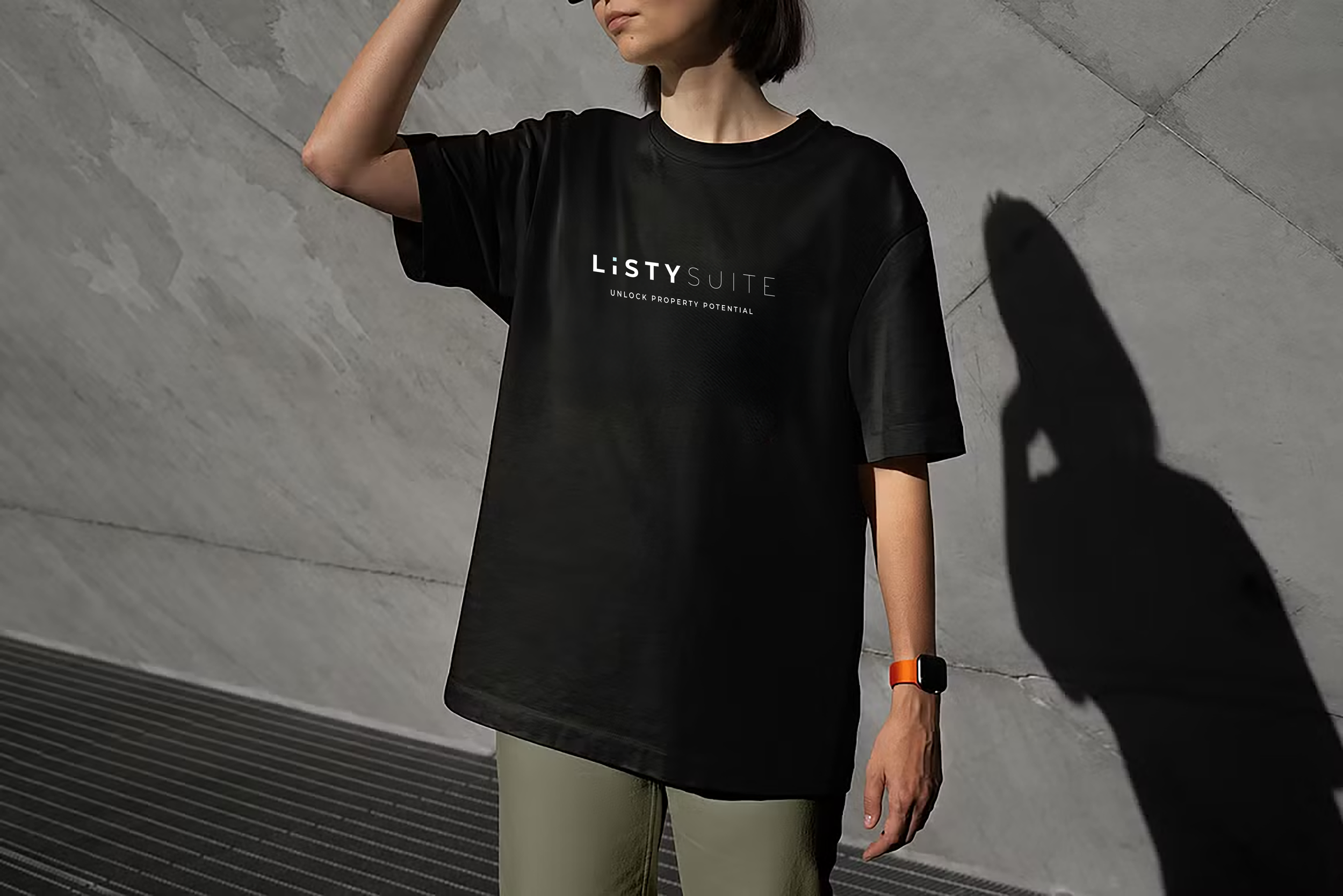 Person wearing a black t-shirt with the text 'LISTY SUITE' and the slogan 'UNLOCK PROPERTY POTENTIAL,' standing against a concrete wall with a shadow cast on the wall.