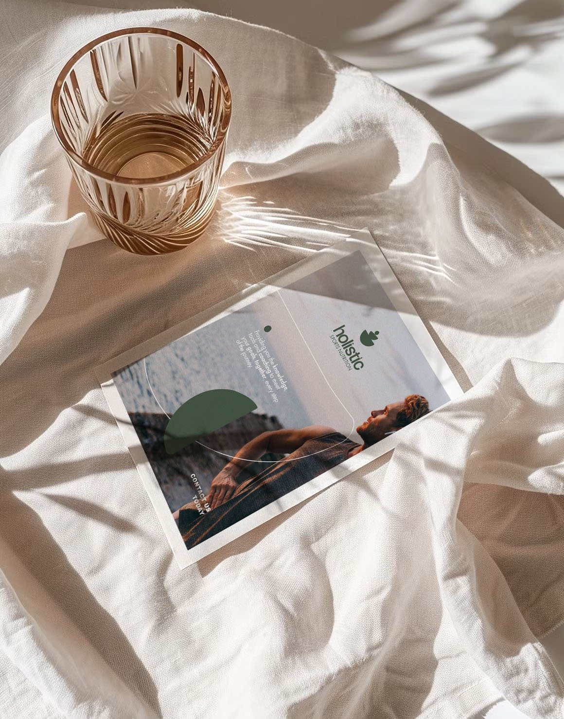 A pink glass of water and a brochure or flyer on a white, crumpled cloth with natural sunlight shining on them.