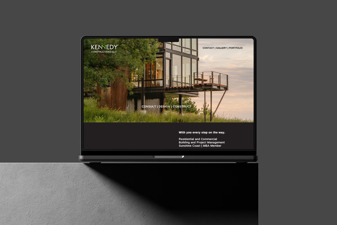 Laptop displaying a website for Kennedy Constructions Queensland with a modern house on the screen, outdoors with a grey concrete background.