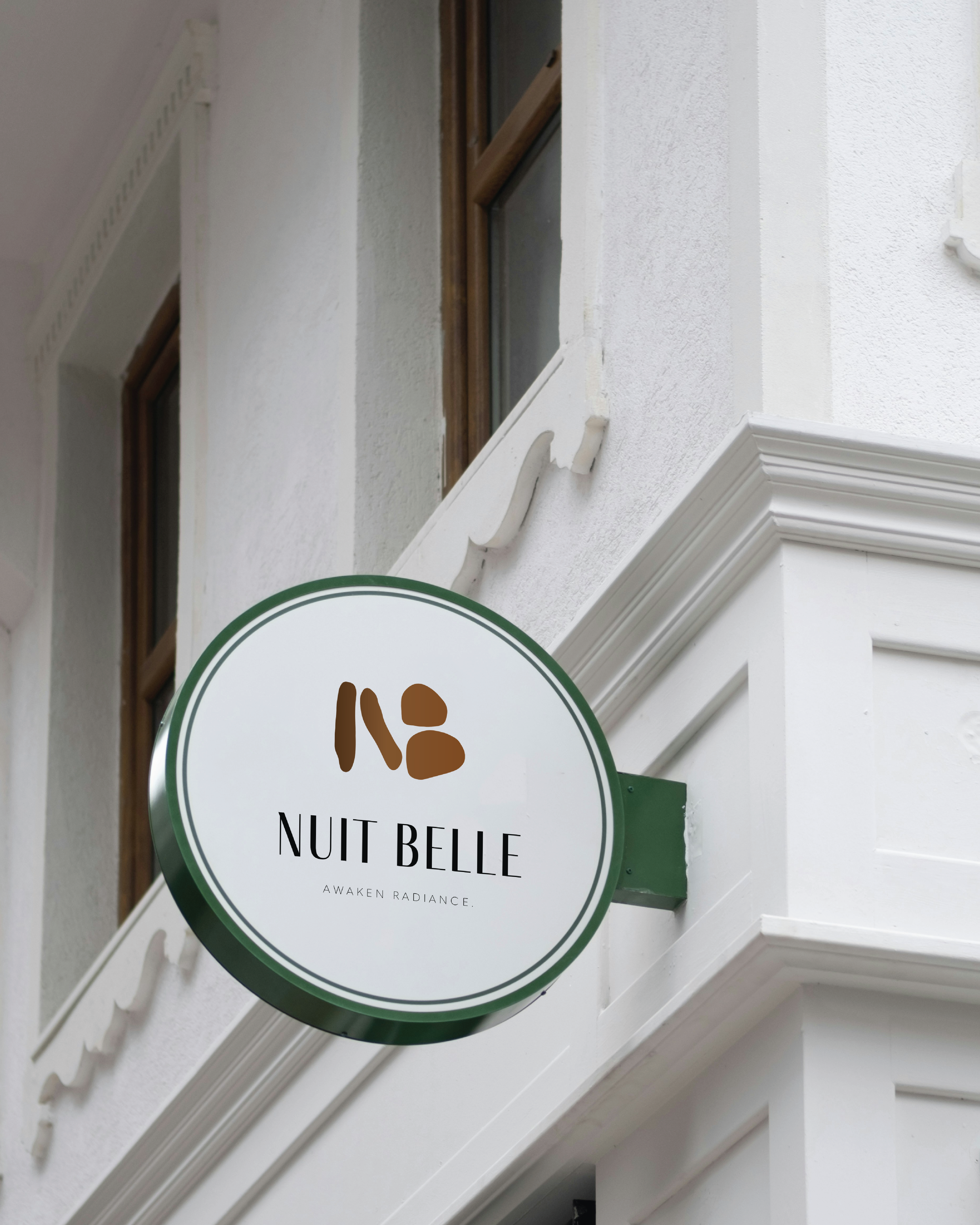 Round sign for 'Nuit Belle' with the tagline 'Awaken Radiance' hanging on a white building exterior.