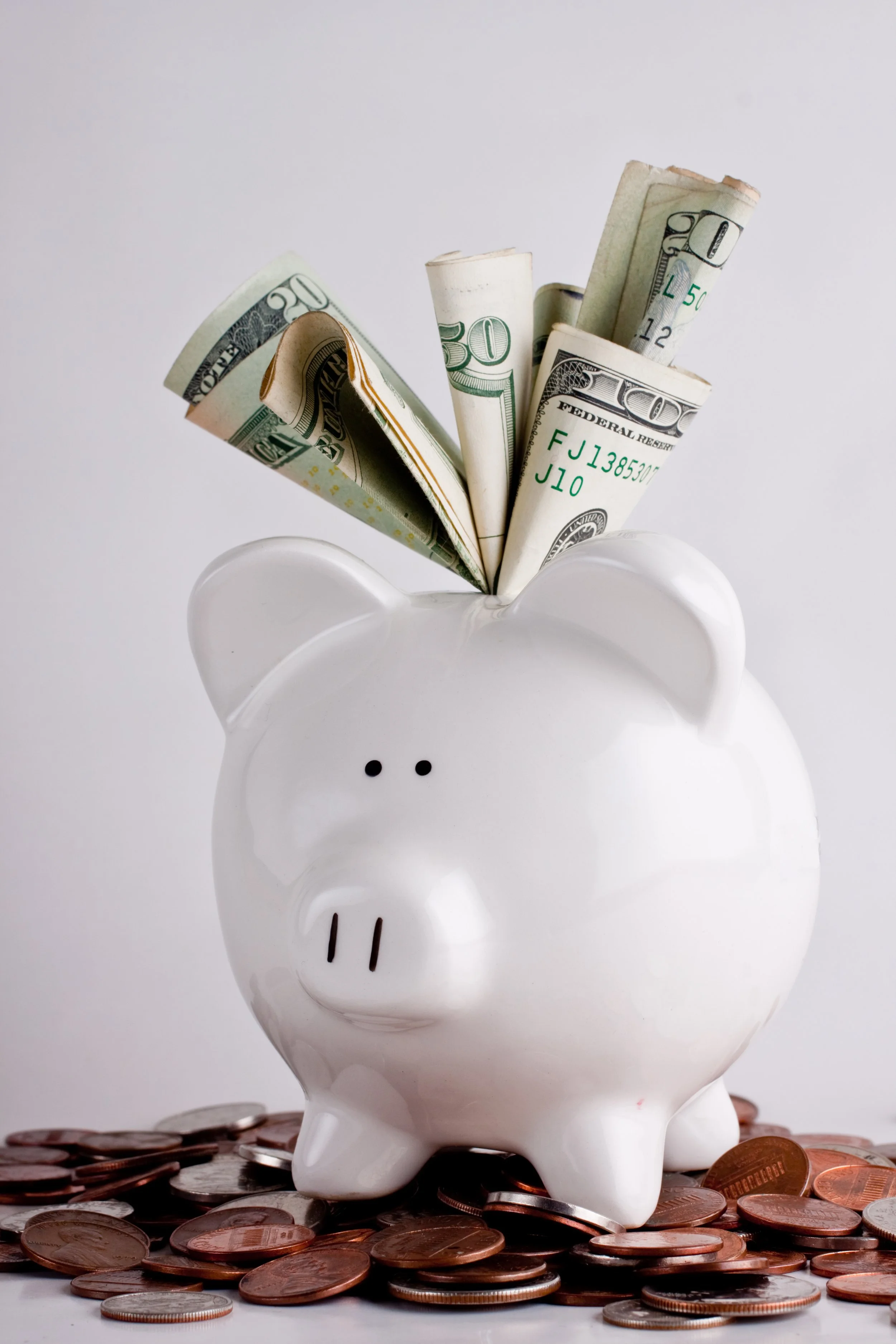 A white piggy bank with rolled dollar bills and coins around it, symbolizing saving money.