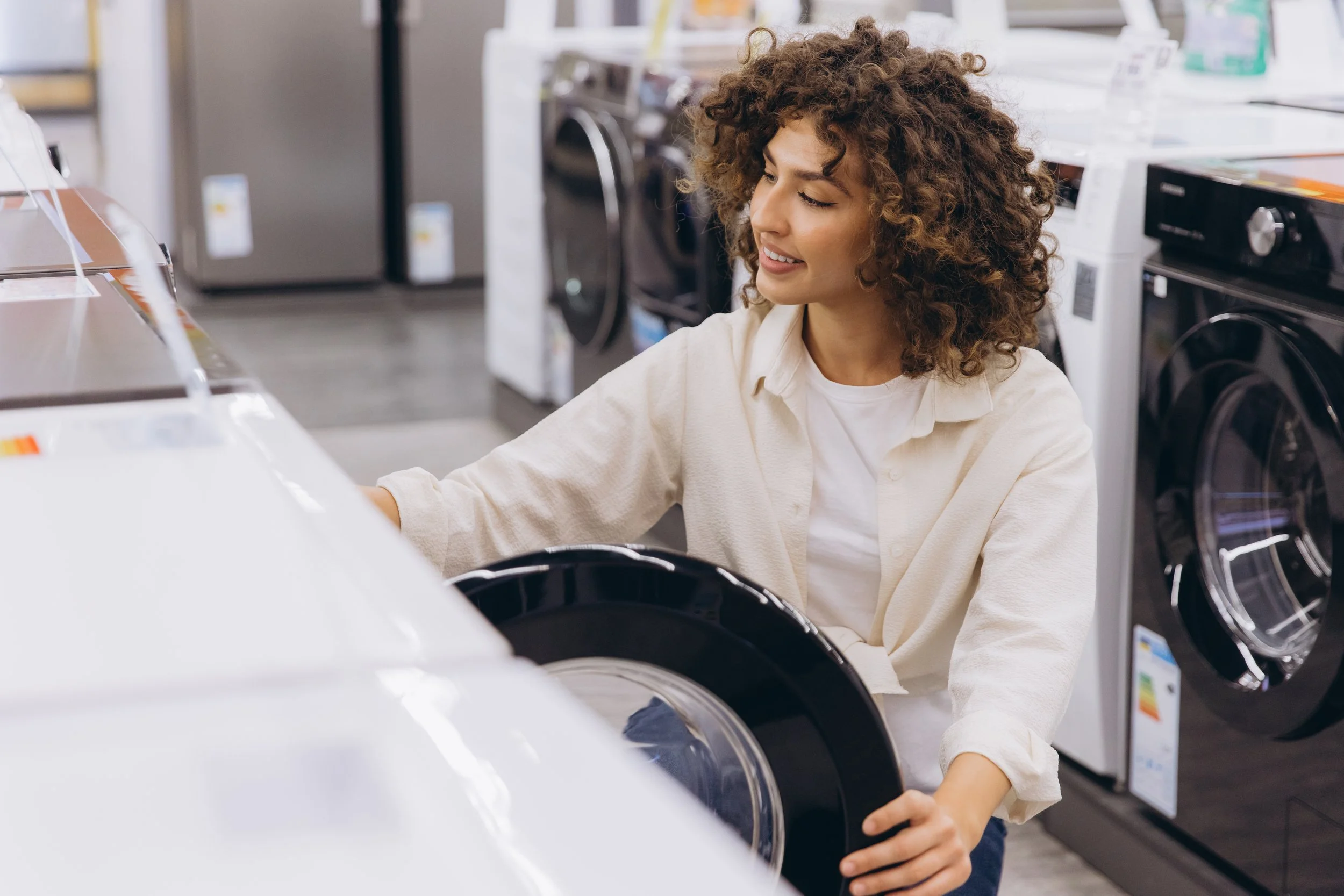 A woman with curly hair shopping in an appliance store, examining a washing machine.