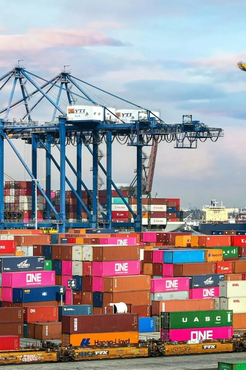 Cargo containers stacked at a port with cranes overhead.
