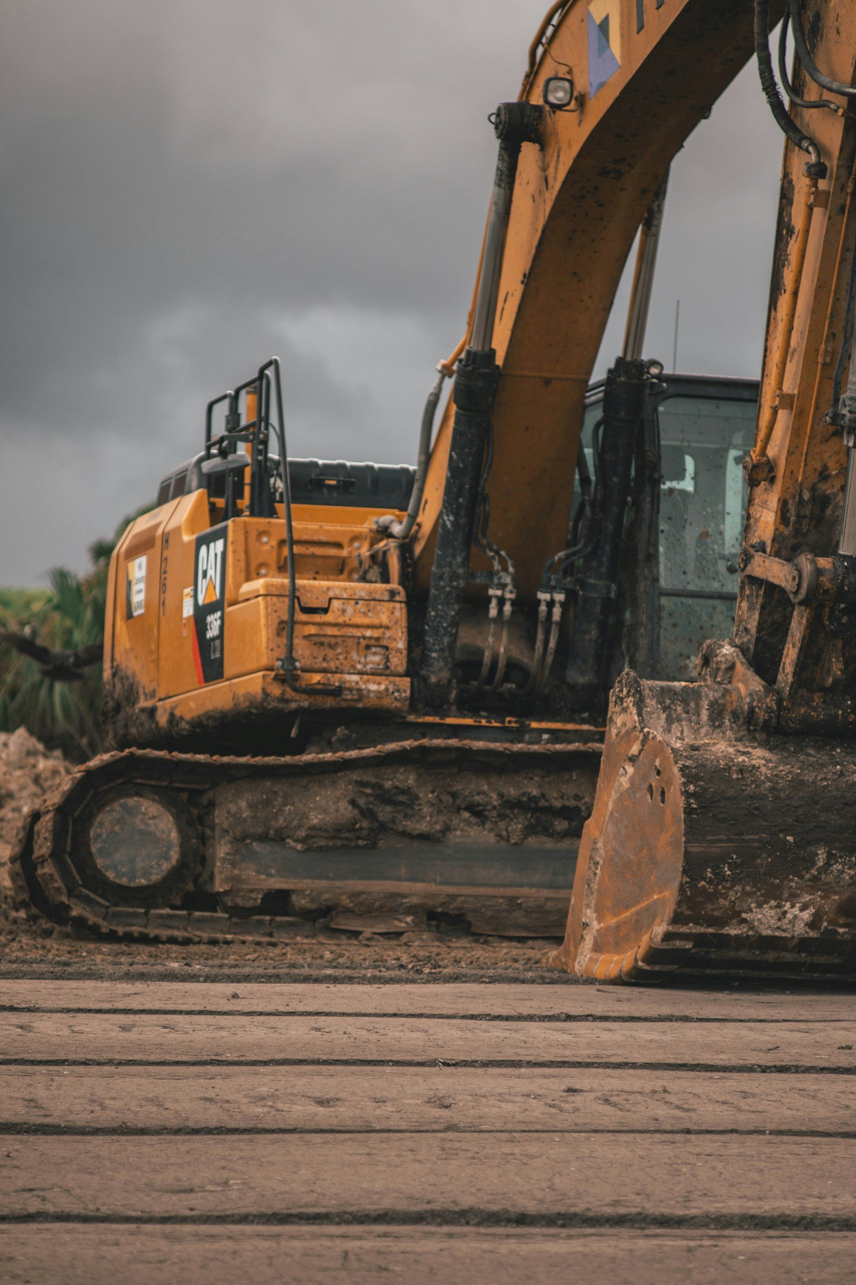 A yellow Caterpillar excavator working on a construction site with a cloudy sky in the background.