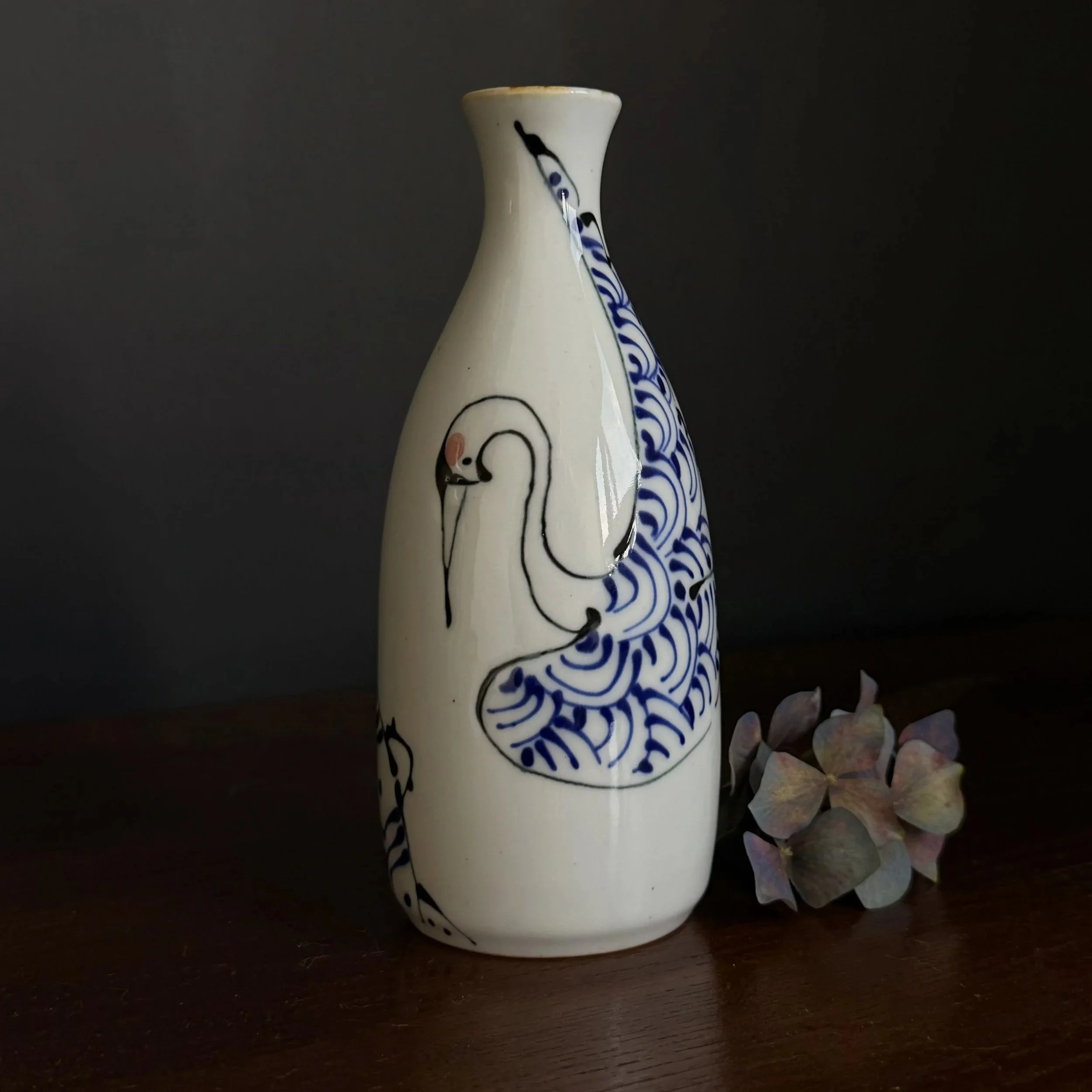 A ceramic sake bottle with a blue and white glaze design of a crane