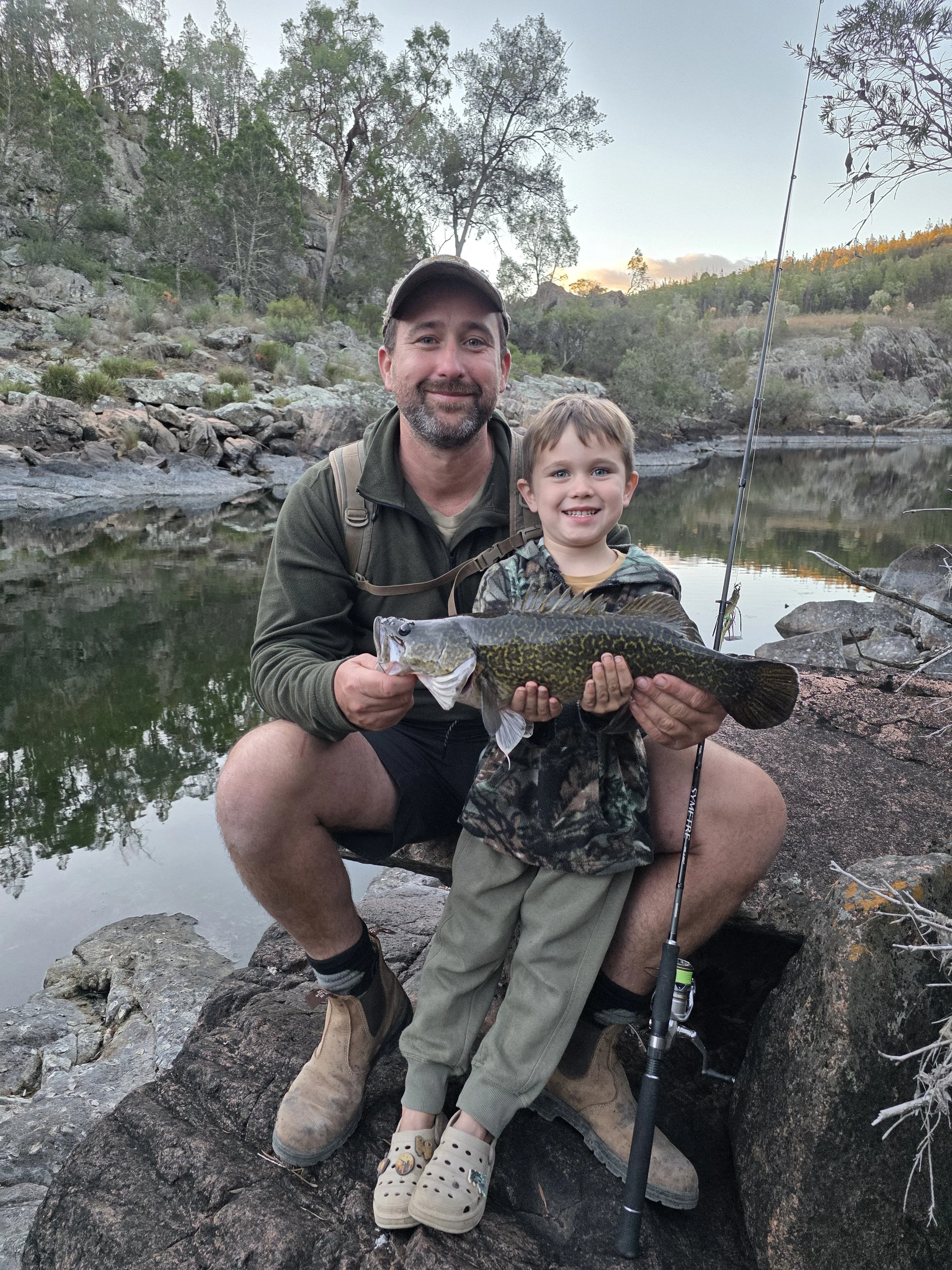 A man and a young boy who has caught his first Murray Cod sitting on rocks by the Severn river NSW