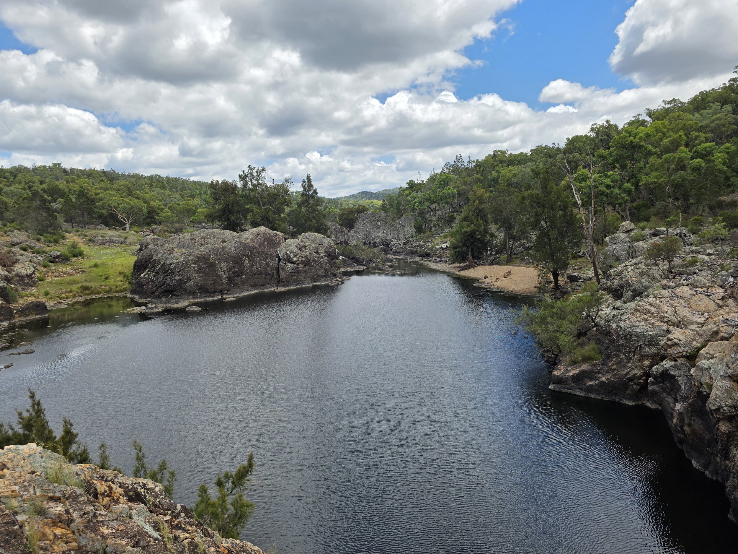 A wide view of a river flowing through a rocky canyon surrounded by green trees under a partly cloudy sky.