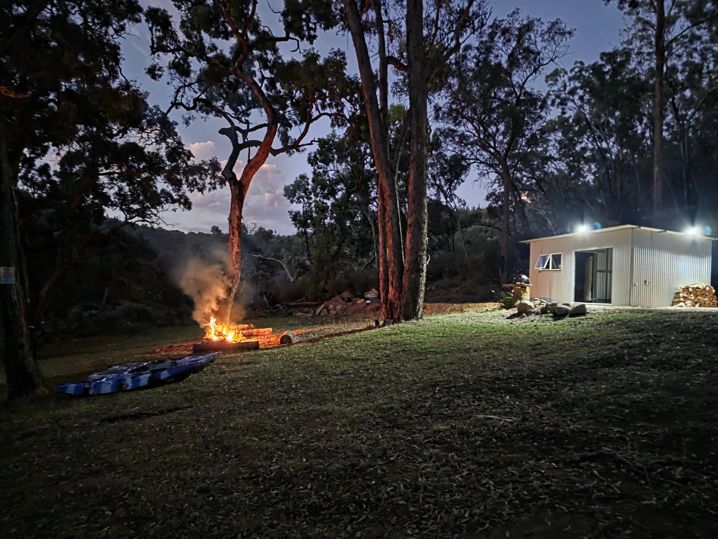 Evening at the Outpost: A crackling campfire and illuminated shelter nestled in the rugged New England timber.