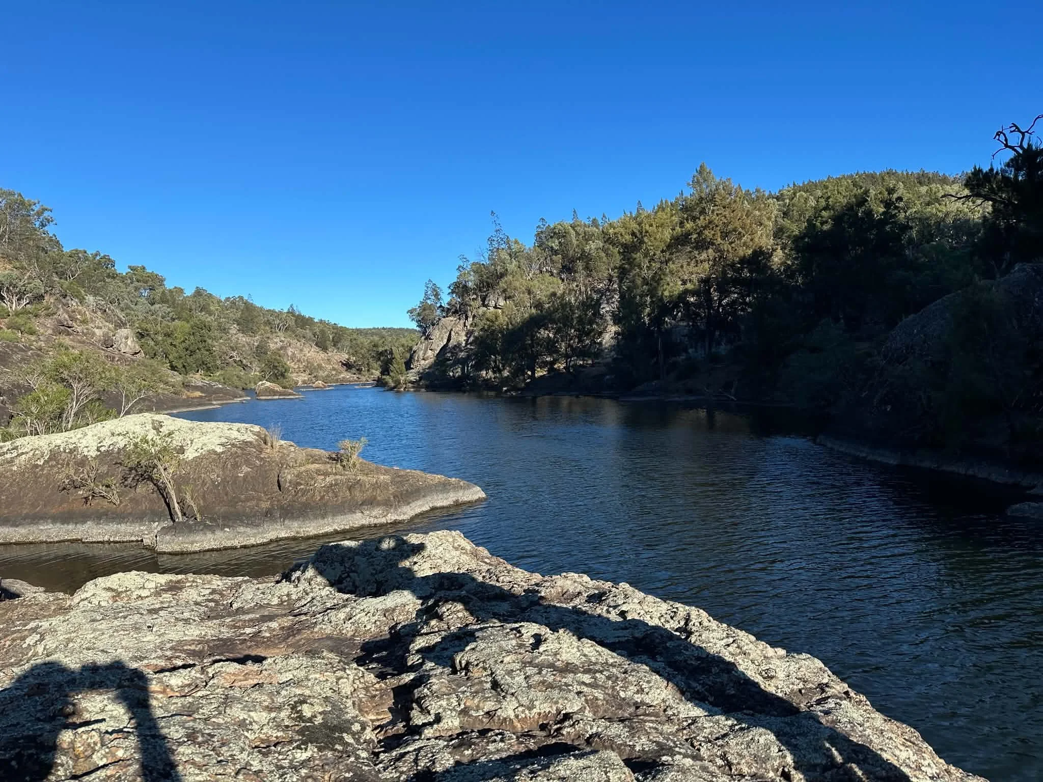 A river flowing through a rocky landscape with trees on either side and clear blue sky overhead.