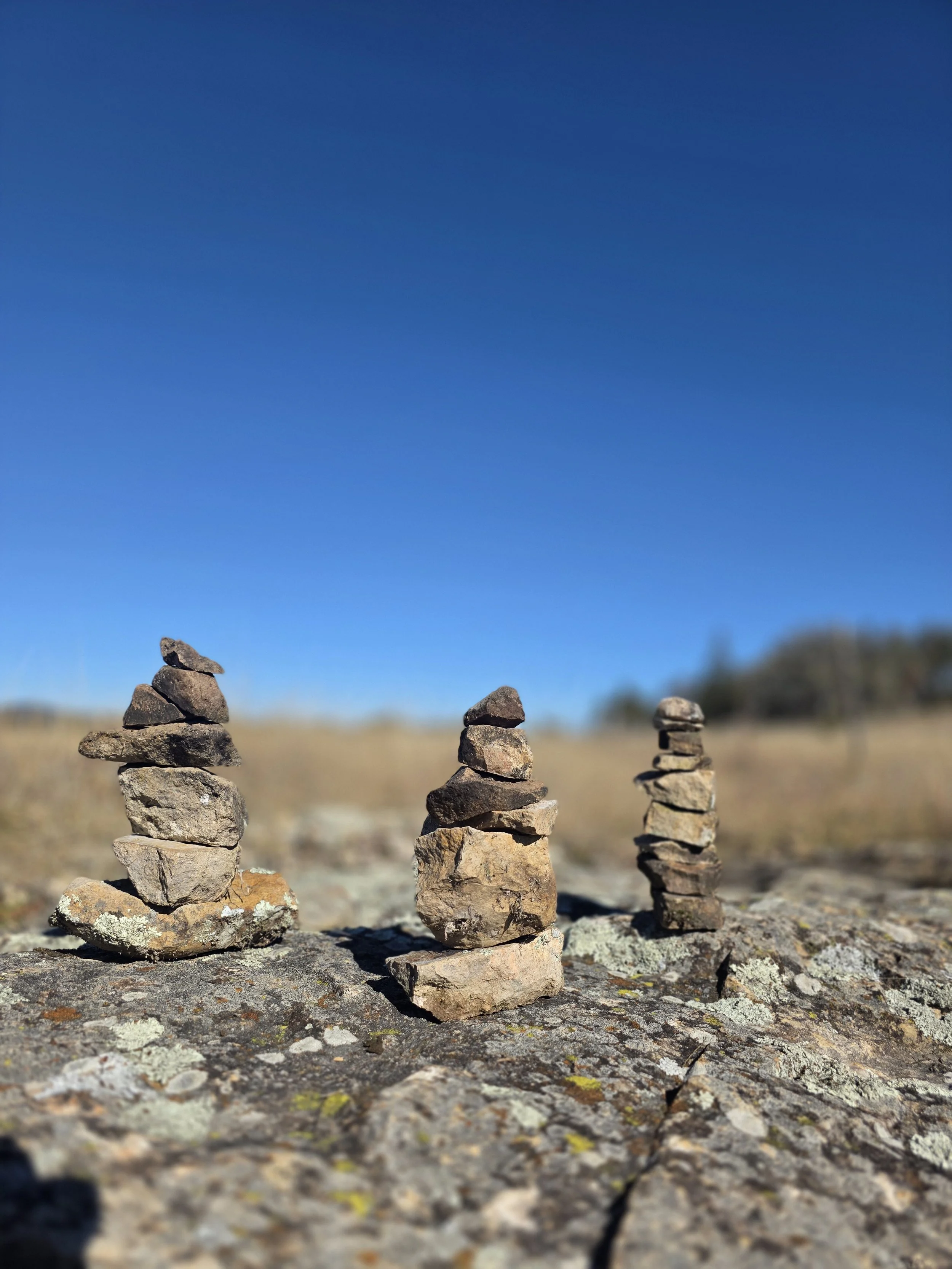 Three small stacks of rocks balanced on a rough rock surface outdoors under a clear blue sky.