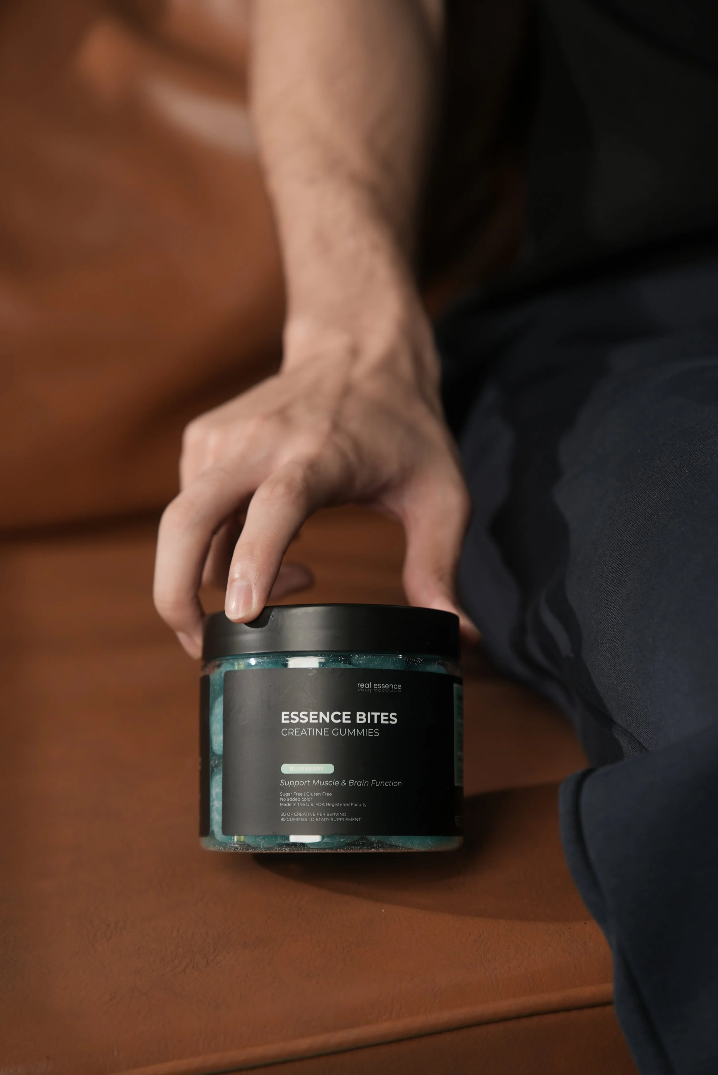A person holding a container of Essence Bites creatine gummies on a wooden surface.