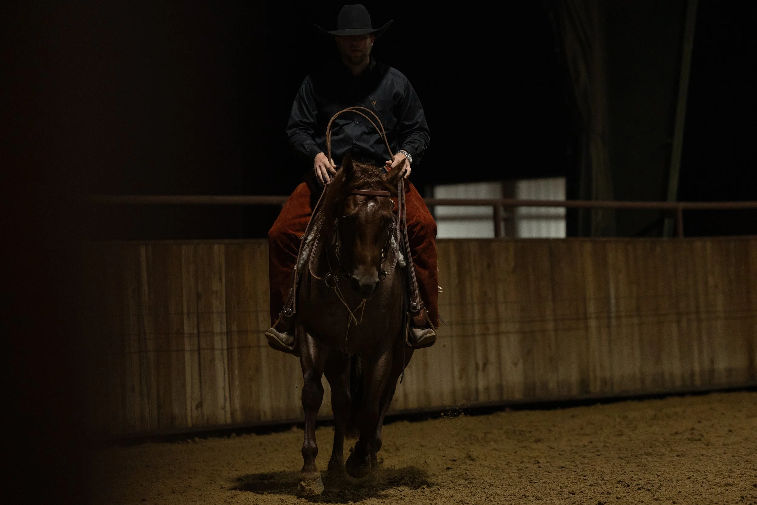 A person riding a horse inside an indoor riding arena.