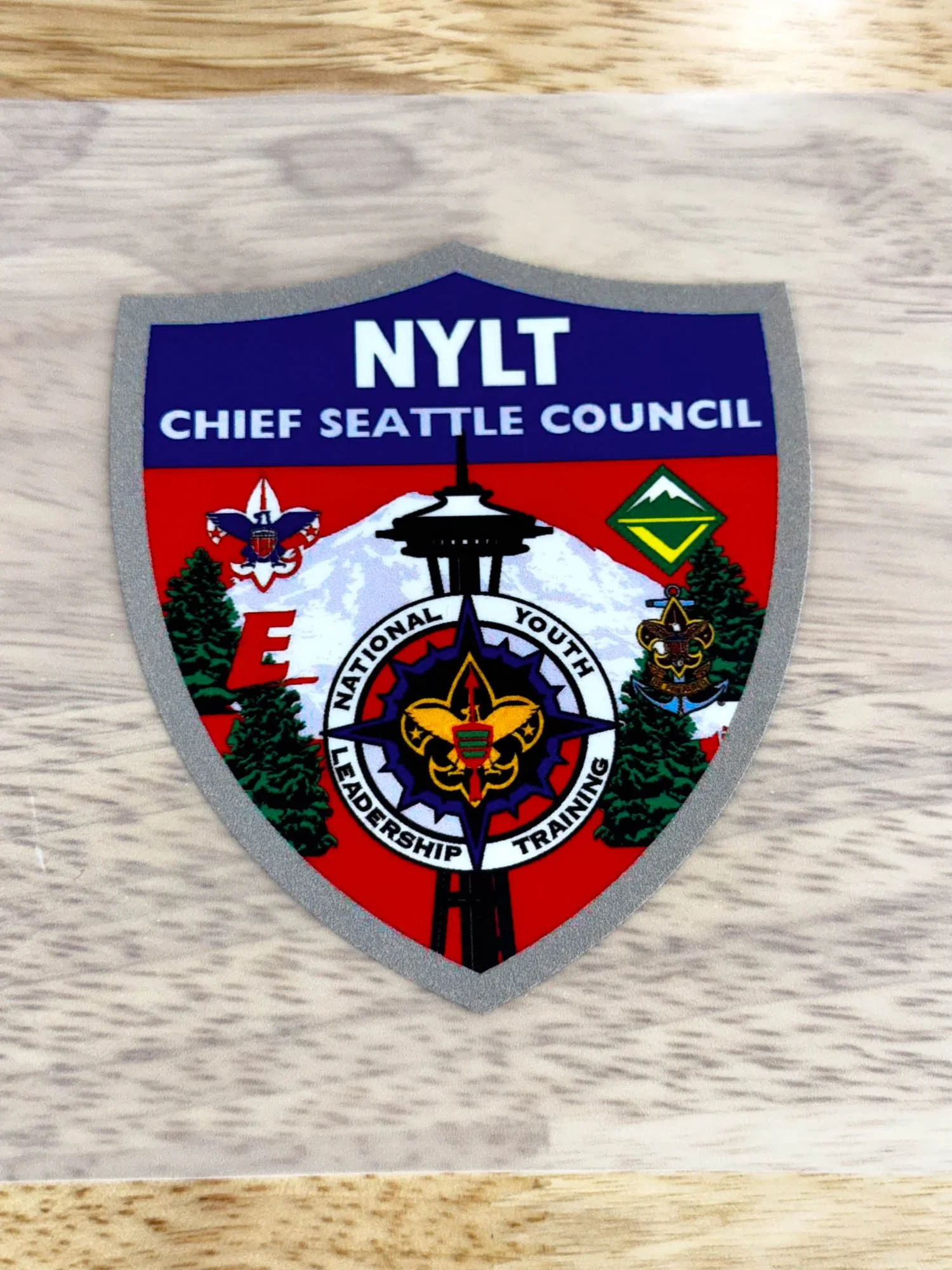A patch or badge for NYLT Chief Seattle Council, featuring the Space Needle, Mount Rainier, trees, and various scouting symbols.