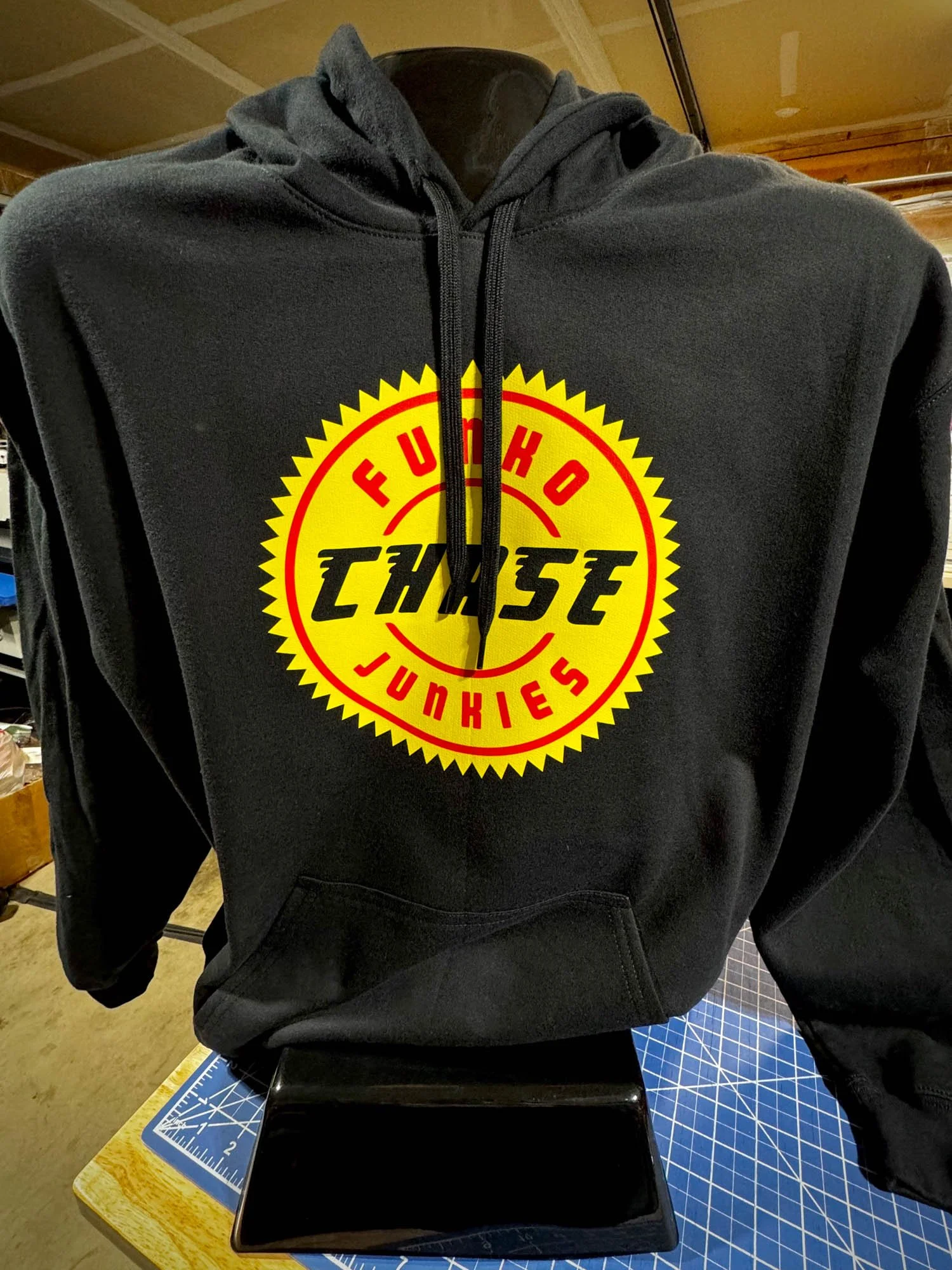 Black hoodie with a yellow, red, and black logo that says 'FUKOH JUNKIES' and 'CHASE' in the center, displayed on a mannequin.