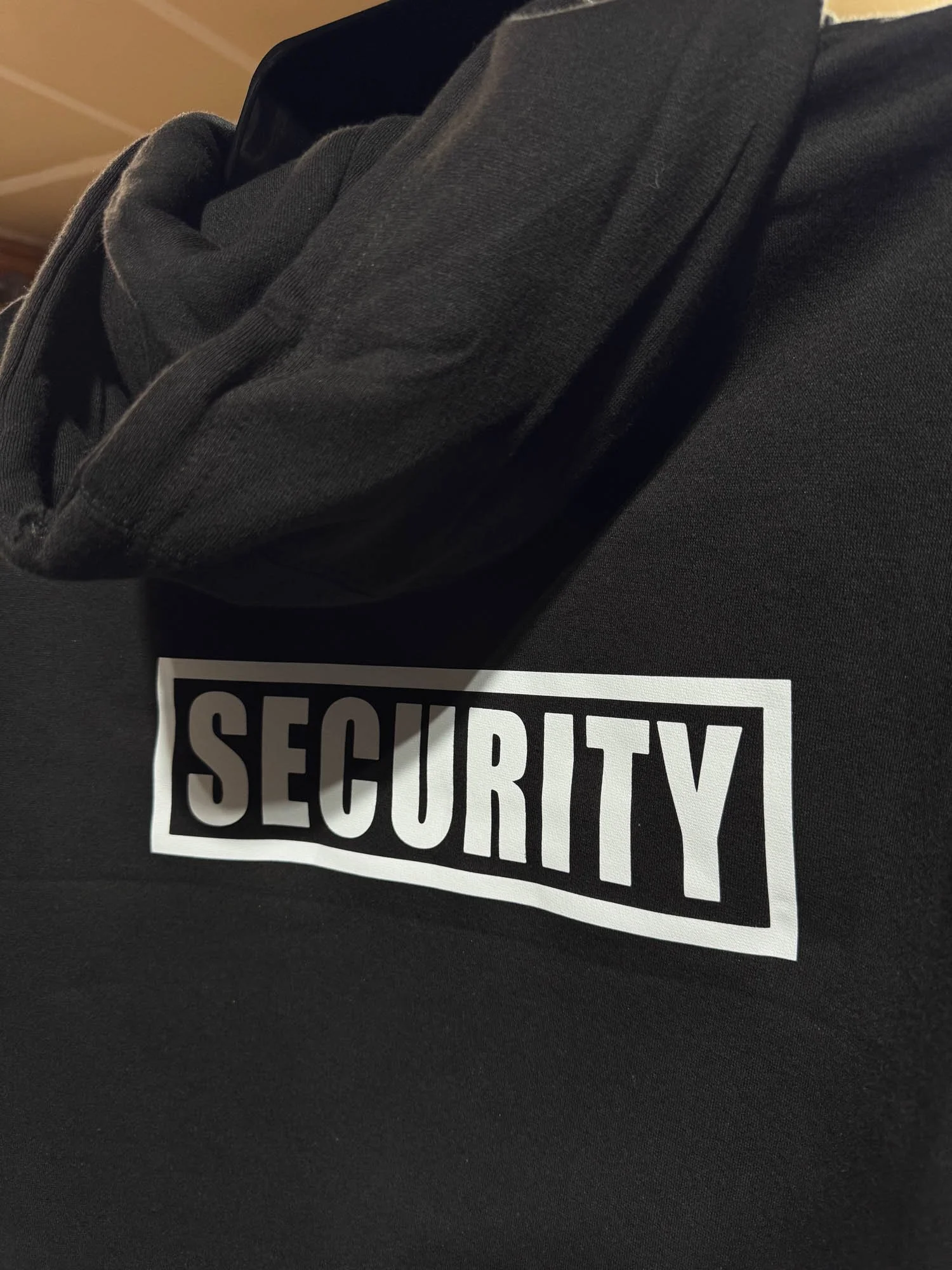 Close-up of a security officer's black uniform with a white security badge on the chest and a neck scarf.