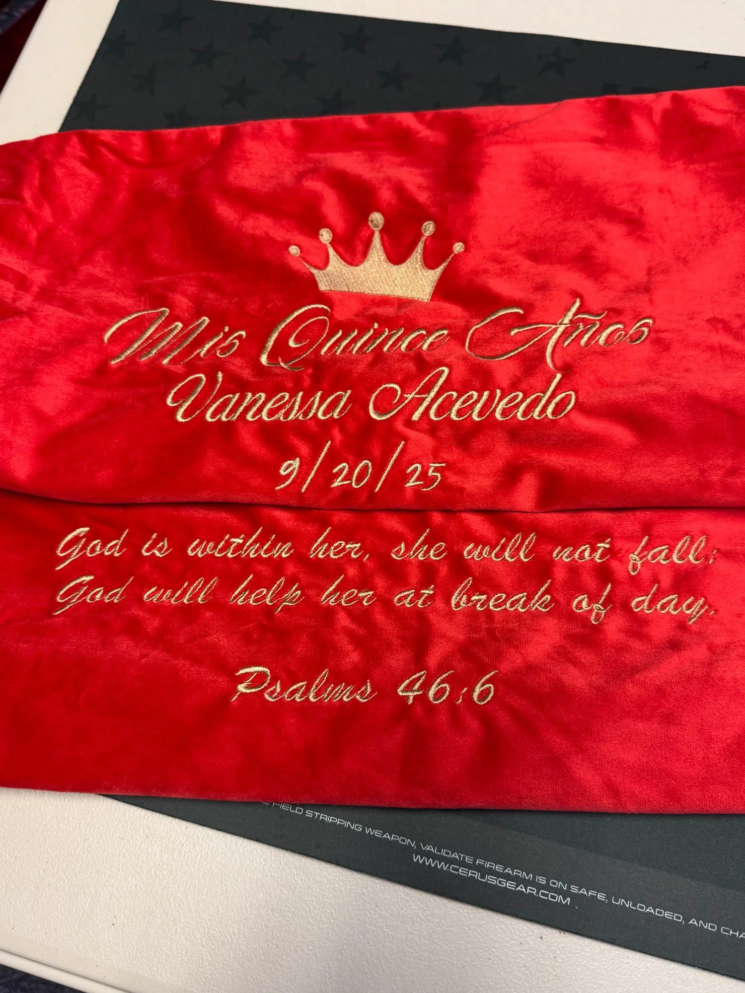Red satin fabric with gold embroidered text and crown, commemorating Miss Quince Años Vanesa Acevedo's 15th birthday on September 20, 2025 with a Bible verse from Psalms 46:6.