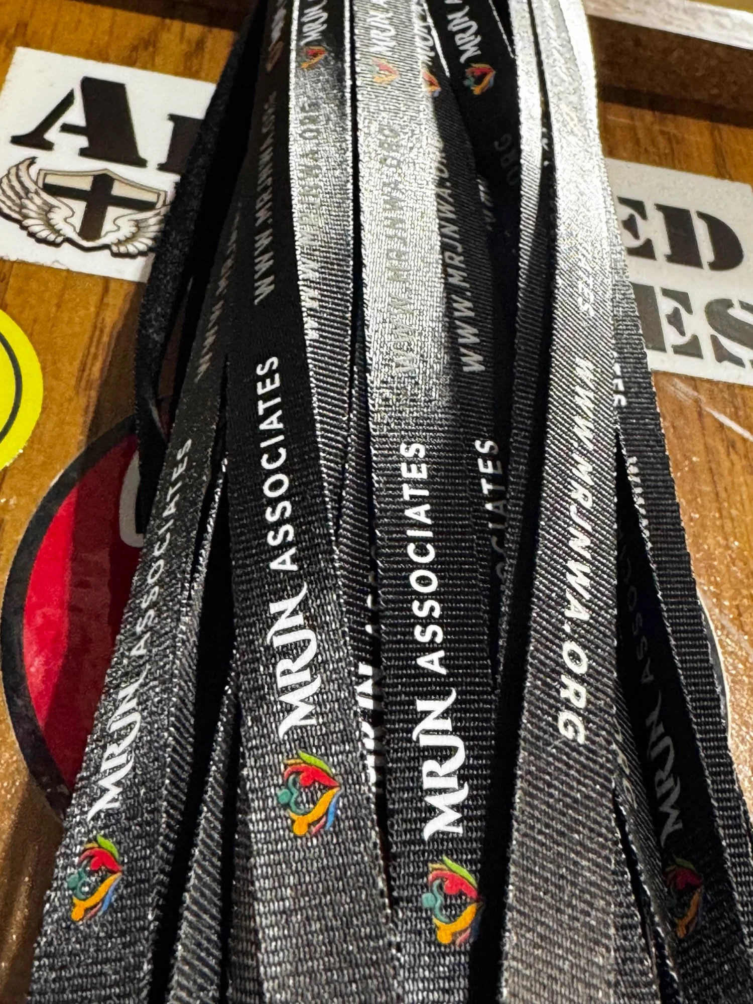 Black lanyards with white text that reads 'NURSN ASSOCIATES' and a multicolored emblem, placed on a wooden surface with stickers nearby.