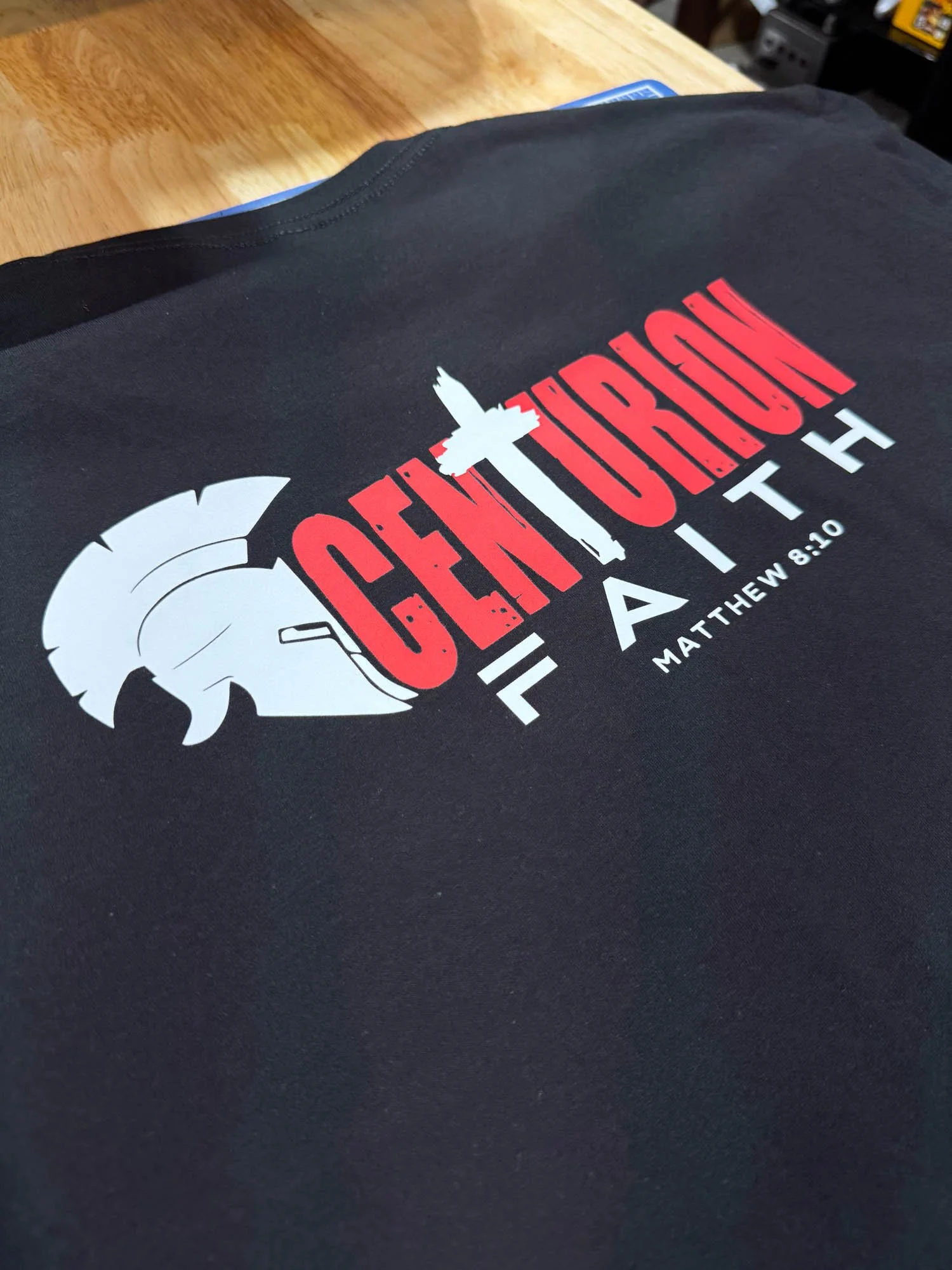 Black t-shirt with graphic design featuring a white Trojan helmet, a gray sword, the words "GENTORIO" in red, and the phrase "FOR A...
MATTHEW 8:10" in white.