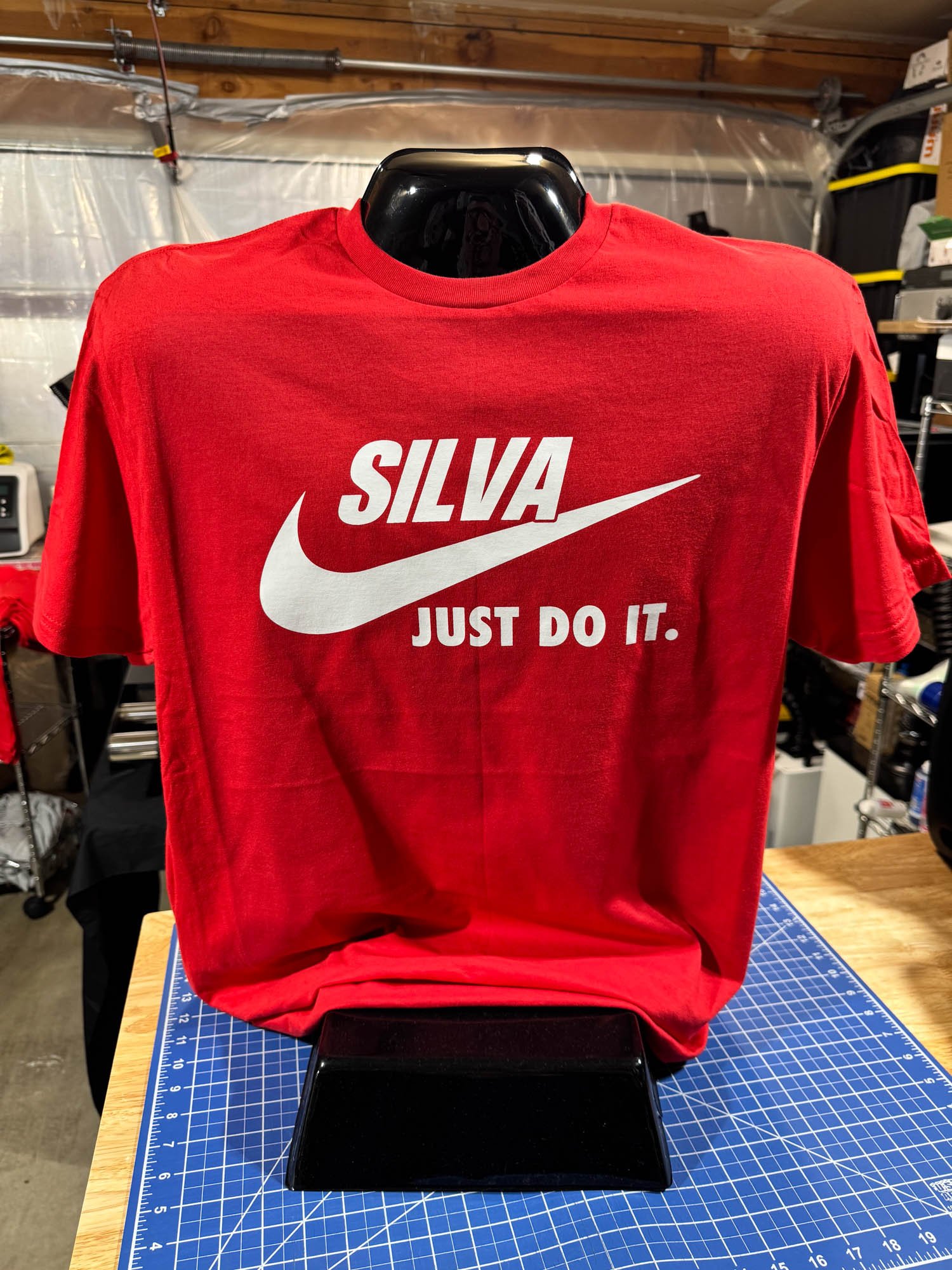 Red T-shirt with Nike logo and the words 'SILVA' and 'JUST DO IT.' displayed on a mannequin in a workshop or storage room.