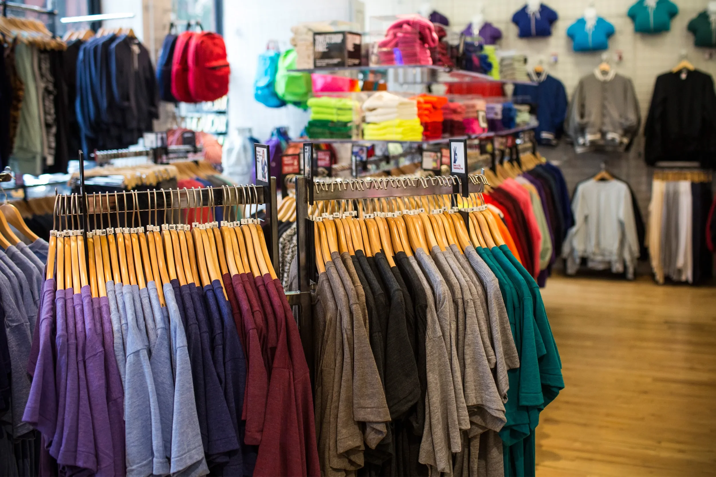 Clothing store with racks of colorful shirts, sweaters, and backpacks display in the background.