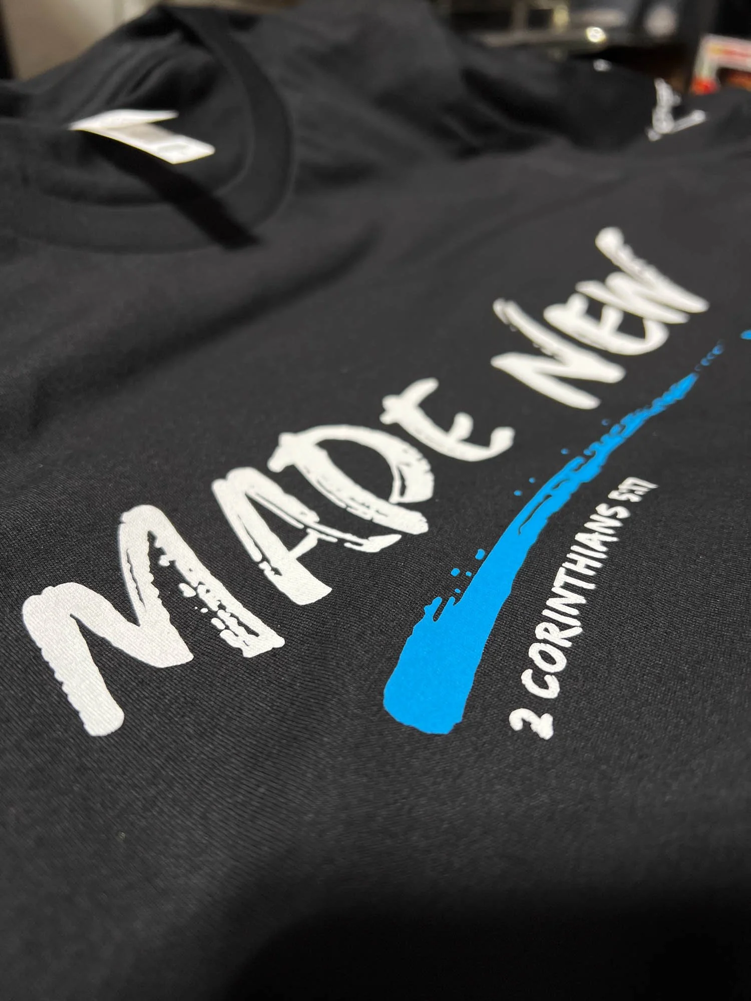 Close-up of a black T-shirt with white text and a blue water splash design, featuring the words 'NATIVE MEN' and '2. RONTHINGS'.