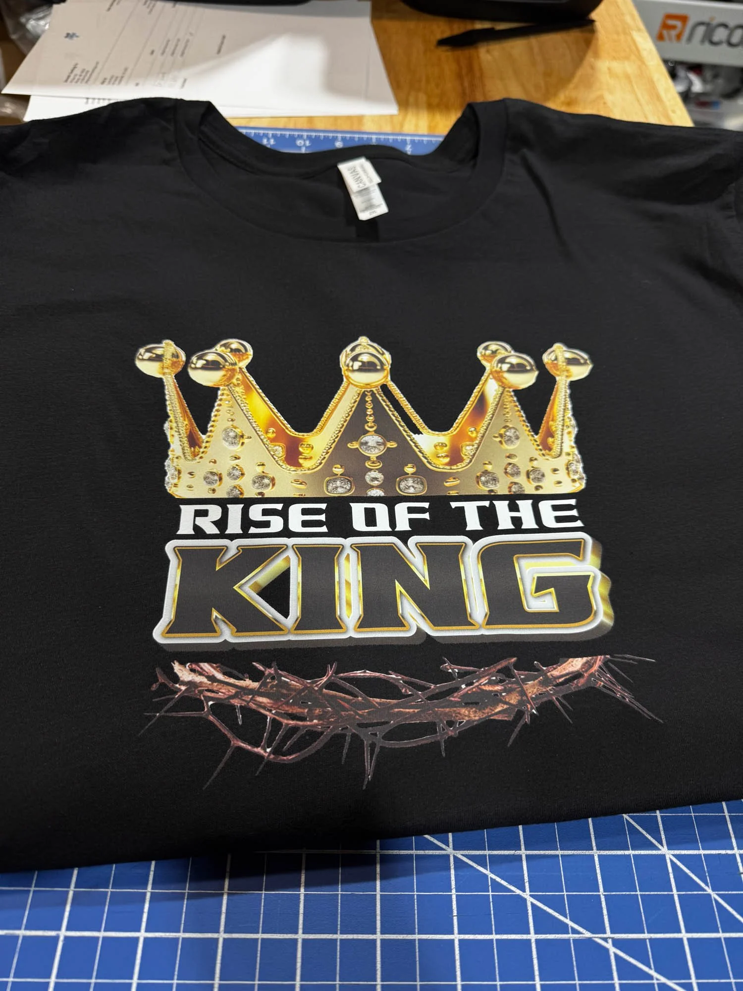 Black T-shirt with a gold crown decorated with jewels, the text 'Rise of the King' below it, and a visually striking crown of thorns underneath.