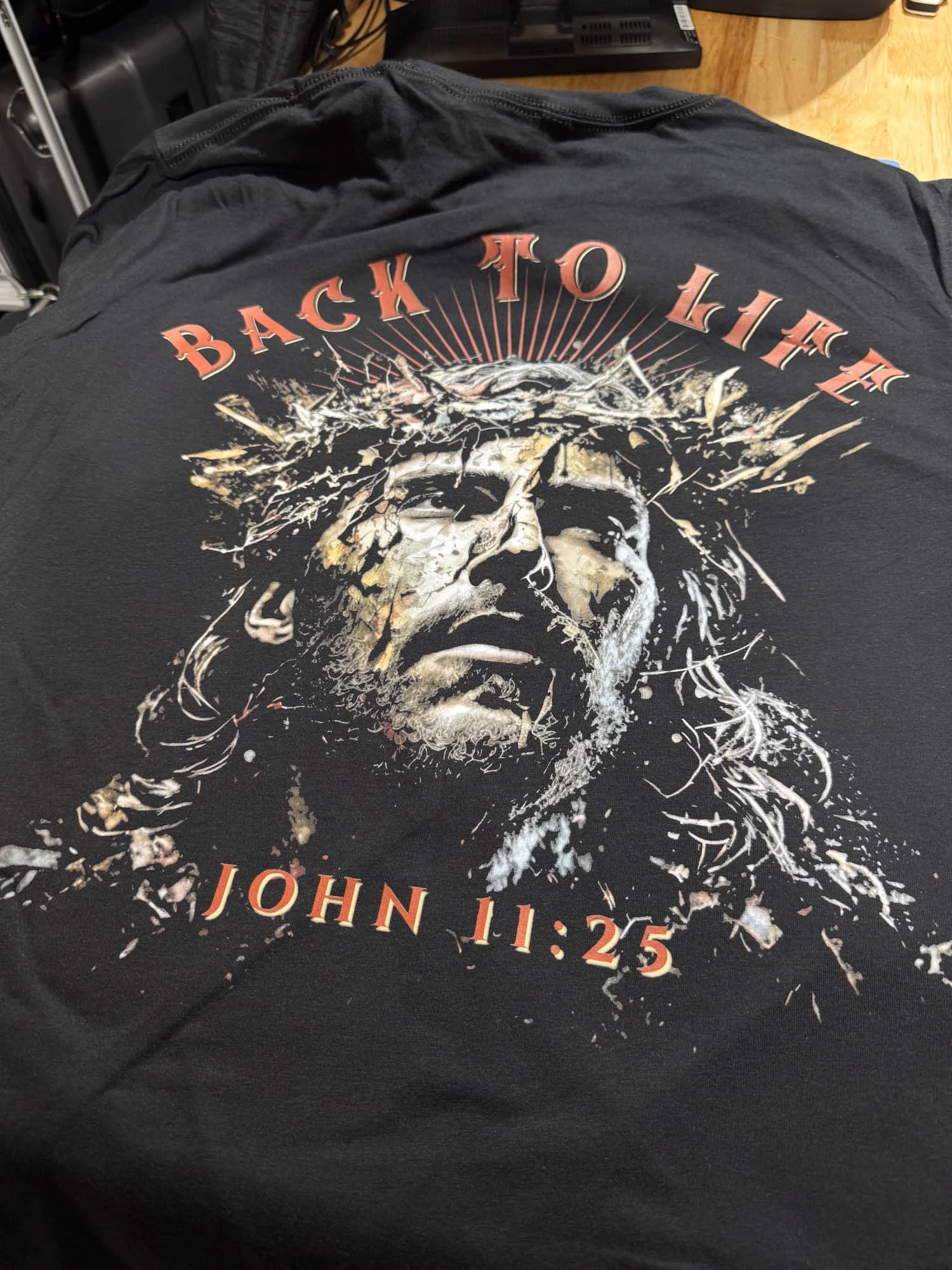 Black T-shirt featuring a graphic of Jesus Christ with a crown of thorns, and the text, 'Back to Life' above the graphic and 'John 11:25' below.