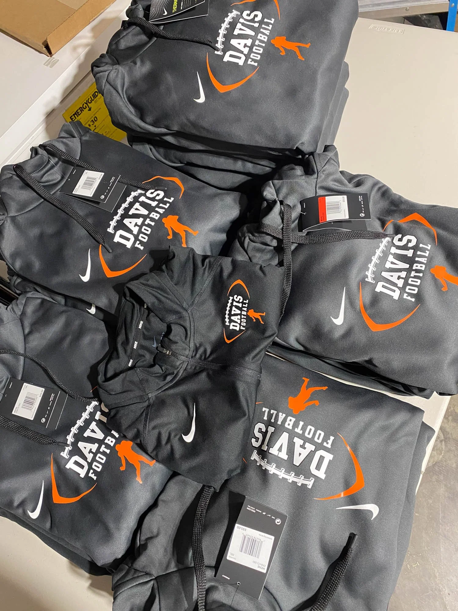 Several gray Nike League Dayz Football hoodies with orange and white logos arranged on a table.
