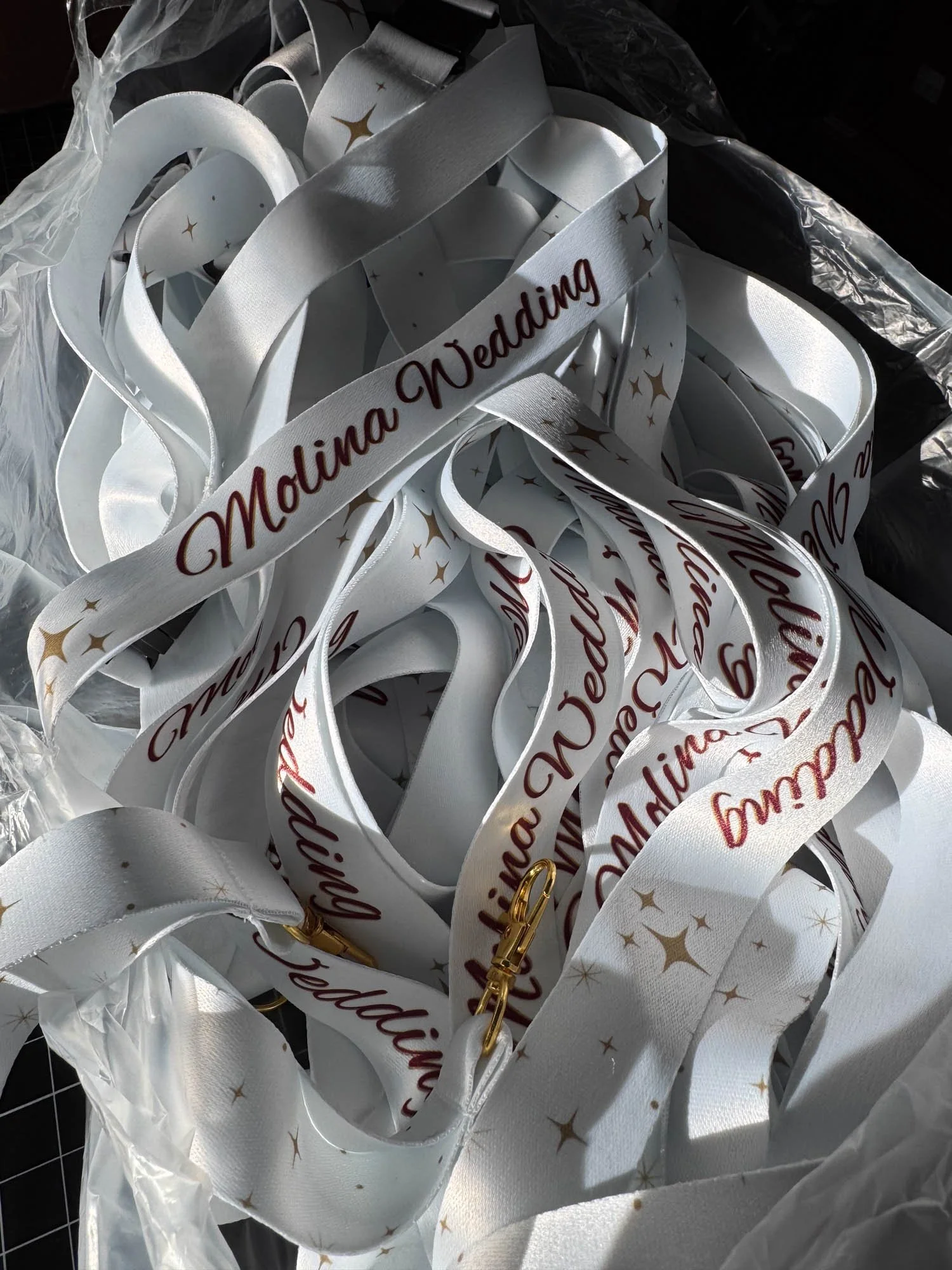 White wedding lanyards with gold stars and maroon text that says 'Molina Wedding,' placed in a transparent plastic bag.