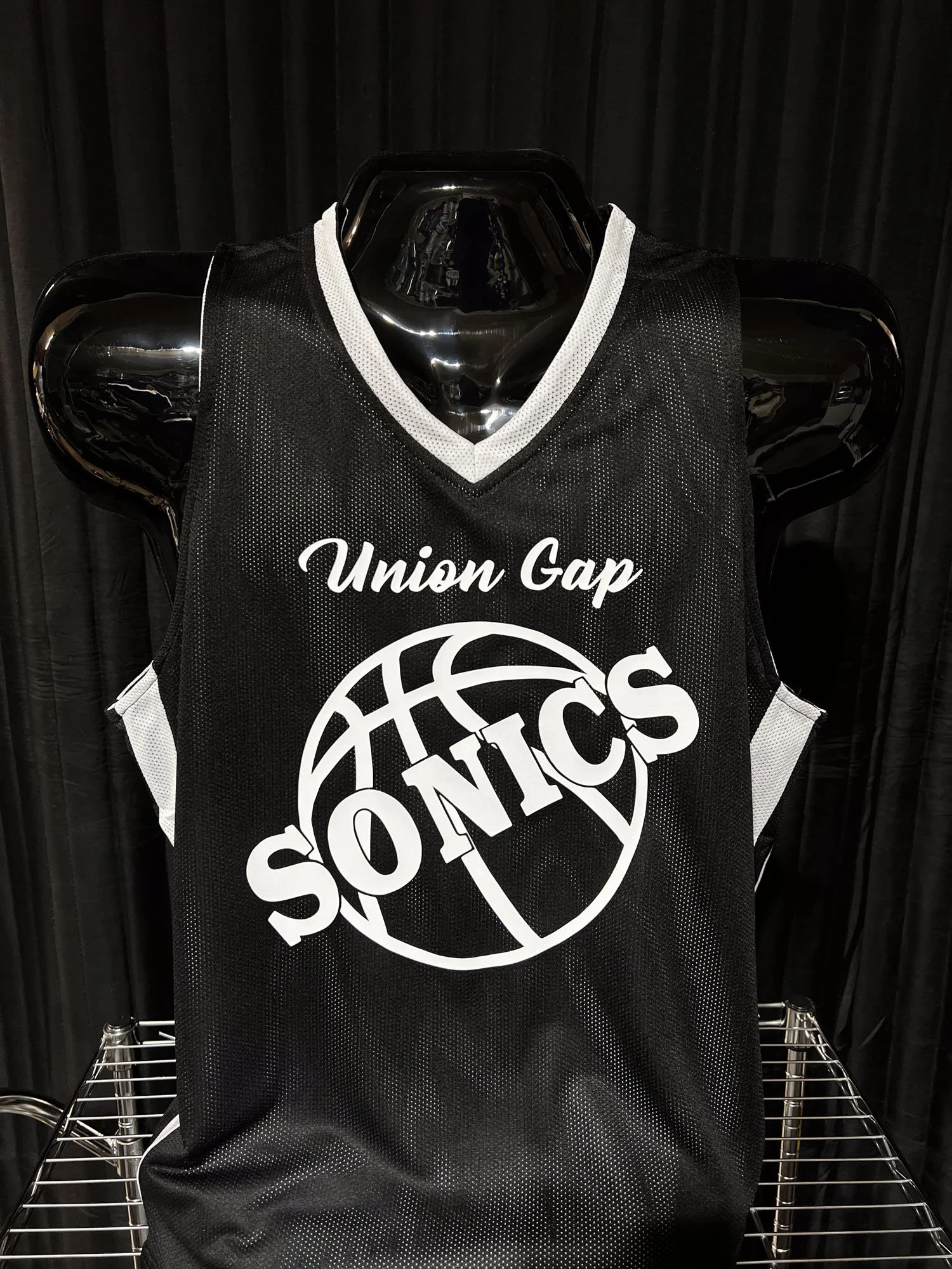 Black basketball jersey with white lettering and logo, displayed on a mannequin. The jersey reads 'Union Gap SONICS' with a basketball logo.