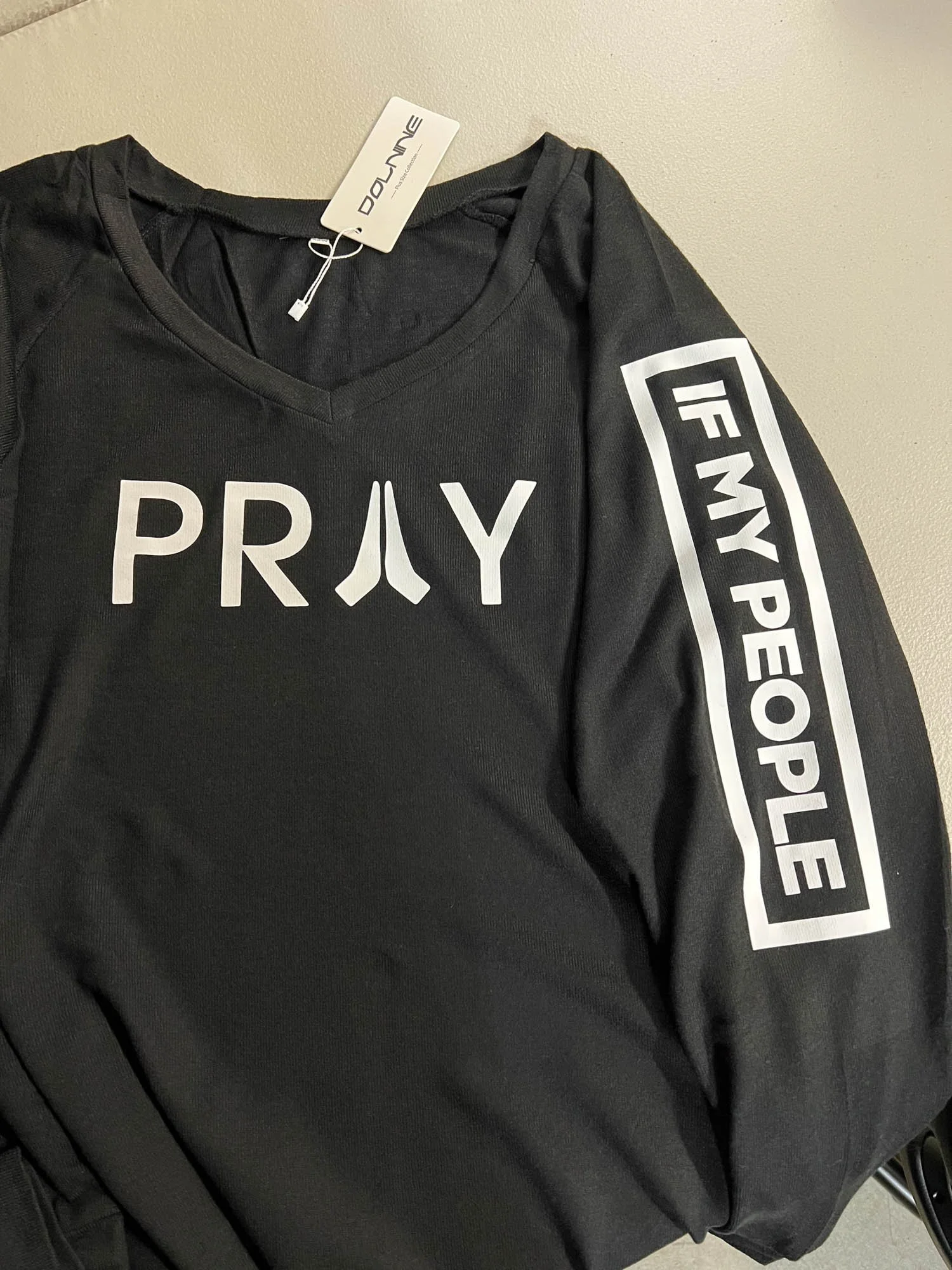 Black long-sleeve shirt with the word 'PRAY' printed on the front in white letters, with the letter 'A' stylized as praying hands. The sleeve has a white patch with the words 'IF MY PEOPLE' printed in black, enclosed in a rectangular border.