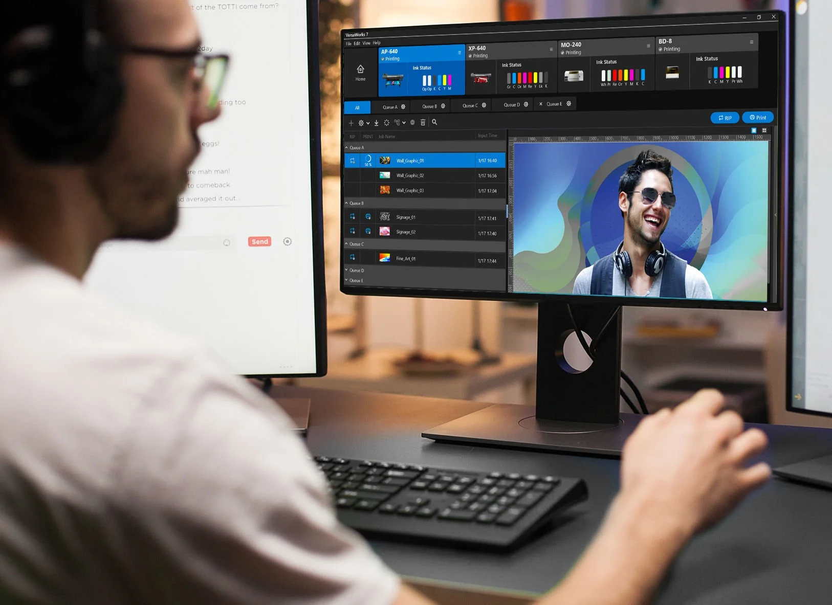 A person working at a computer with dual monitors, one displaying a video editing or graphic design software and the other showing a document. The person is using a keyboard and mouse, and the main monitor shows a cheerful man wearing sunglasses and headphones.