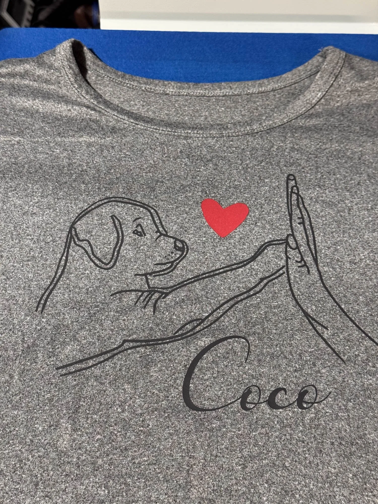 Gray T-shirt with a line drawing of a dog looking at a red heart and text saying 'Coco'.