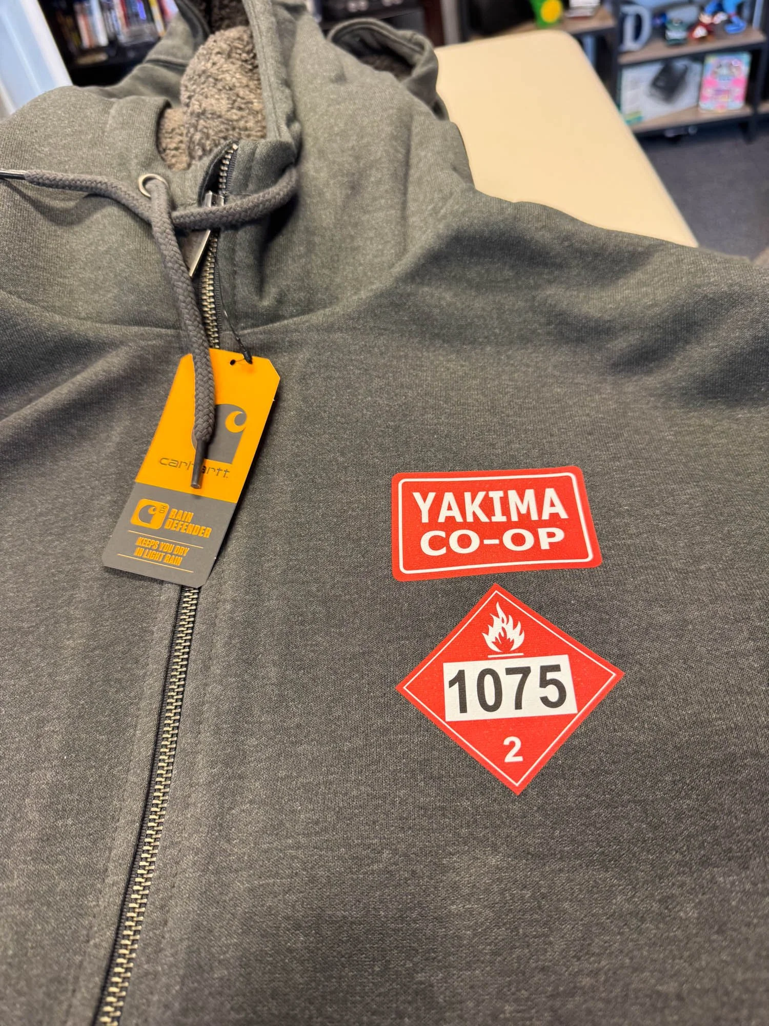 Gray hoodie with Carhartt tags and safety patches on the chest reading 'YAKIMA CO-OP' and hazardous material labels with the number 1075.