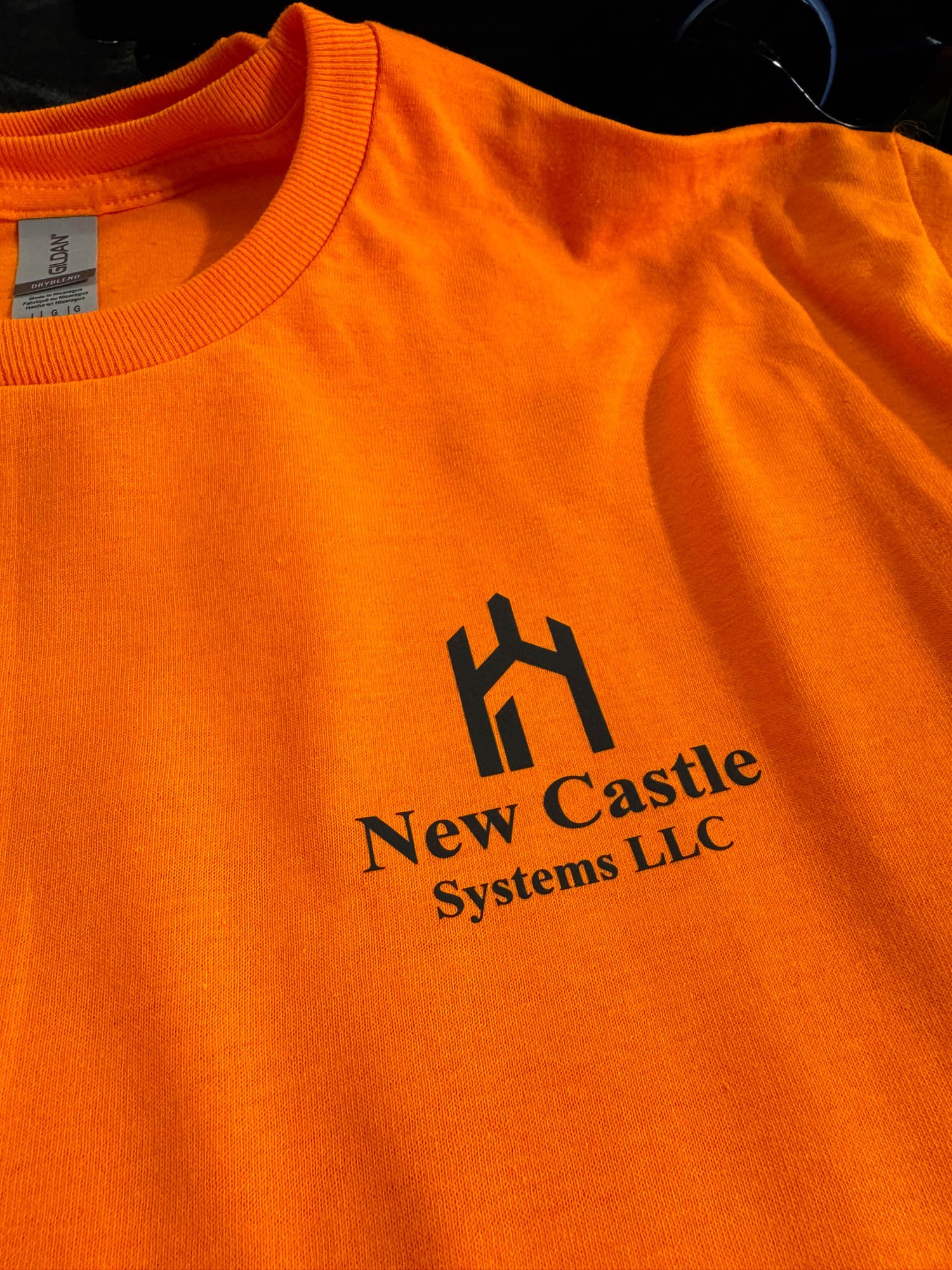 Orange T-shirt with black logo and text that reads 'New Castle Systems LLC'.