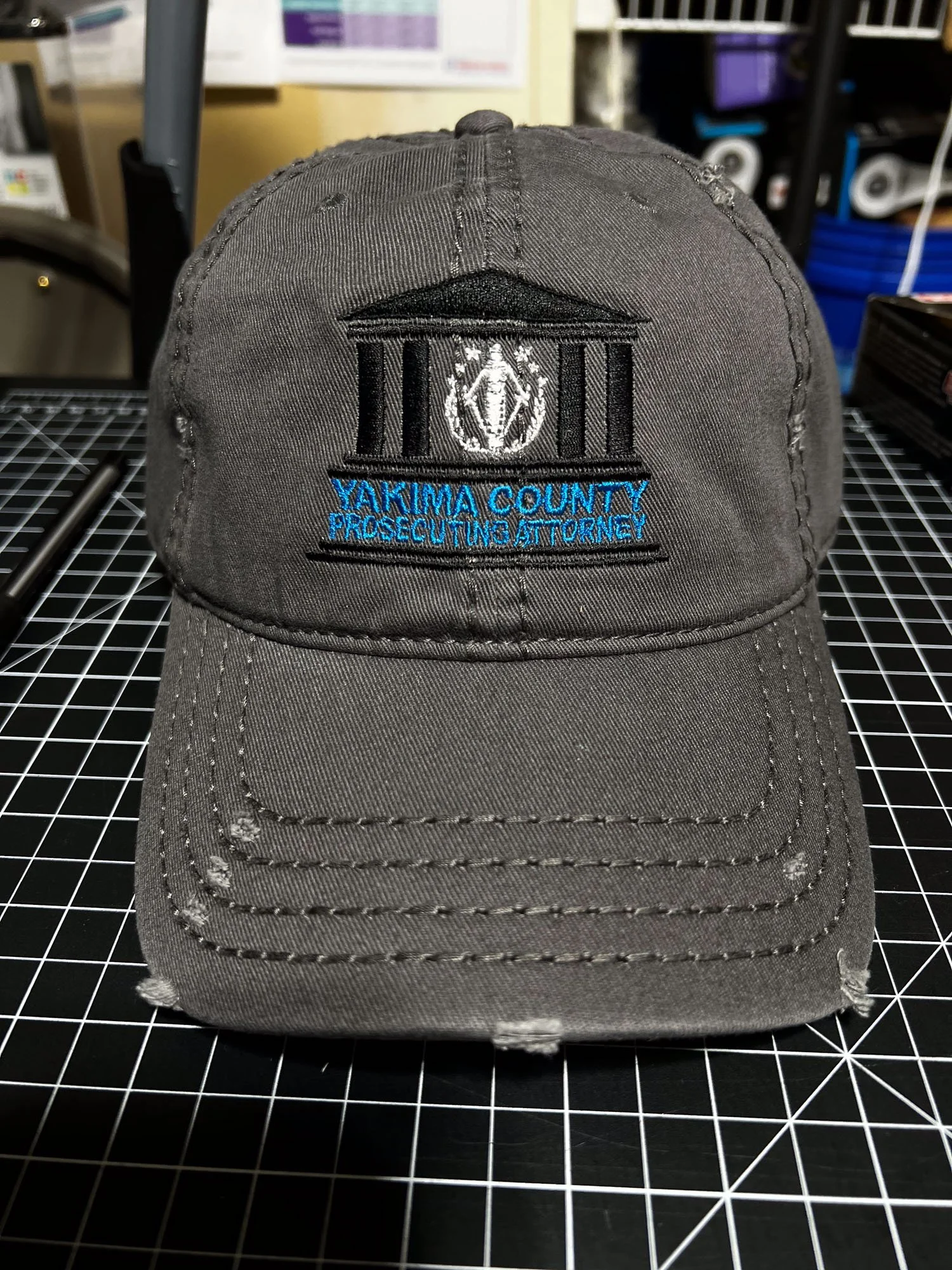 Gray baseball cap with embroidered patch reading 'YAKIMA COUNTY PROSECUTING ATTORNEY' and a courthouse image on the front.