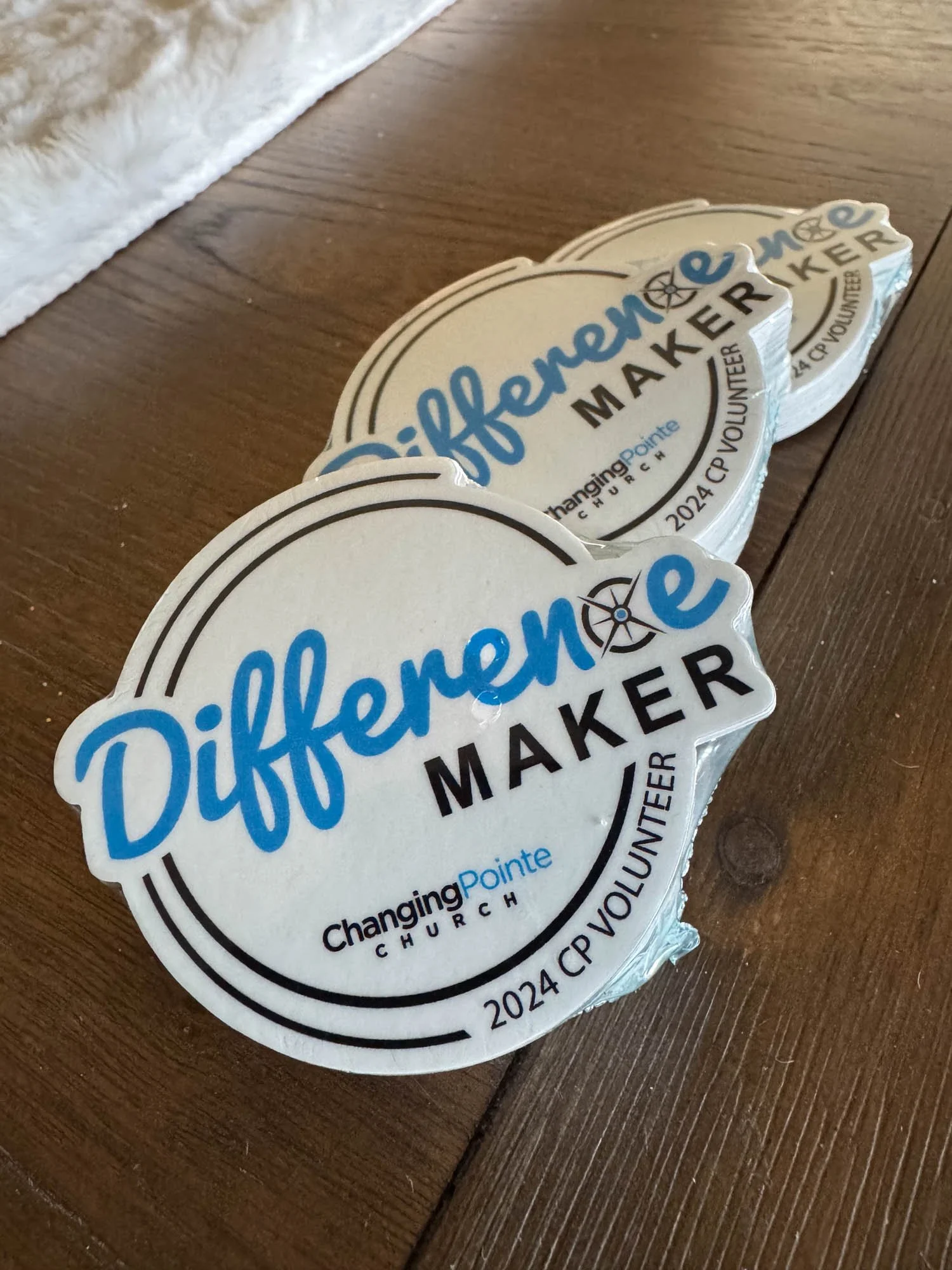 Three stickers on a wooden surface that say 'Difference Maker' with the logo and name of Changing Pointe Church, along with the year 2024 and the note 'CP Volunteer'.