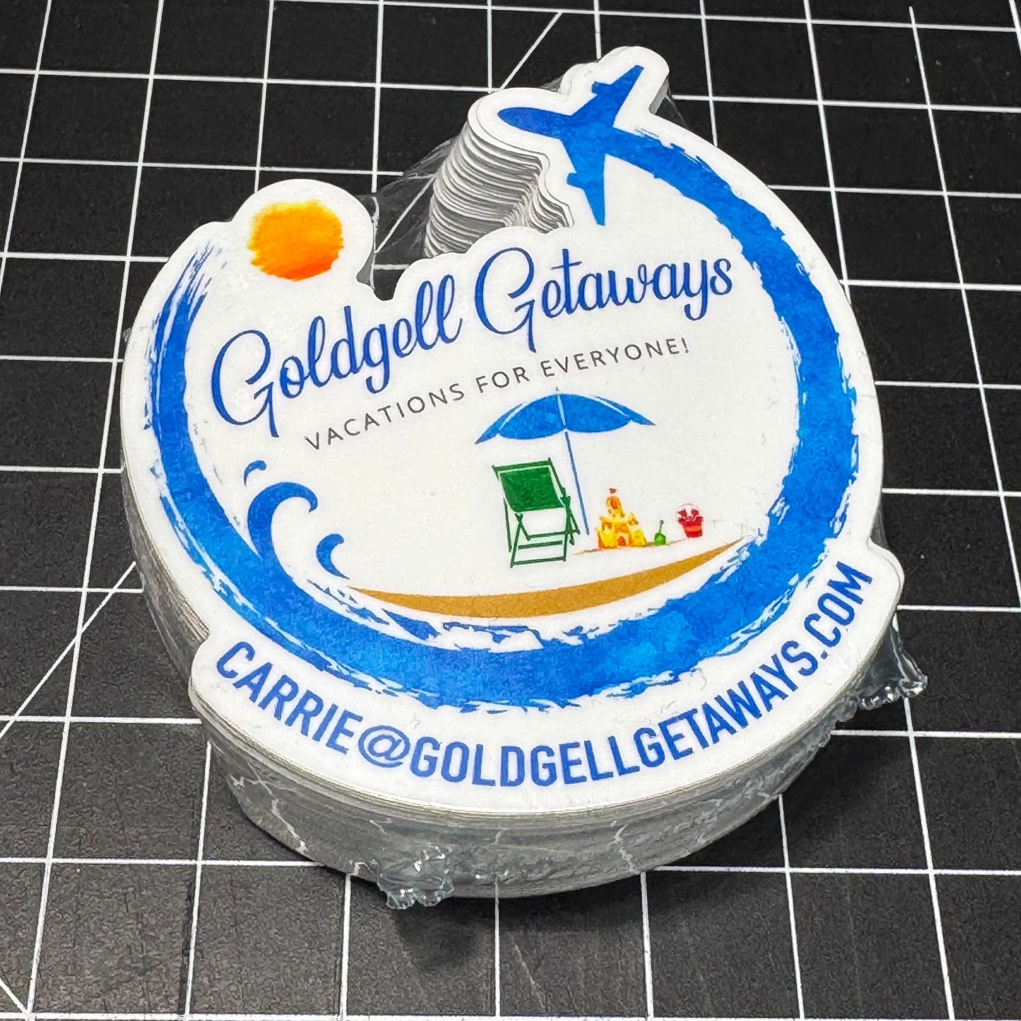 A stack of round stickers for Goldgel Vacation Getaways, featuring the company's logo with a beach scene, umbrella, beach chair, and sun.